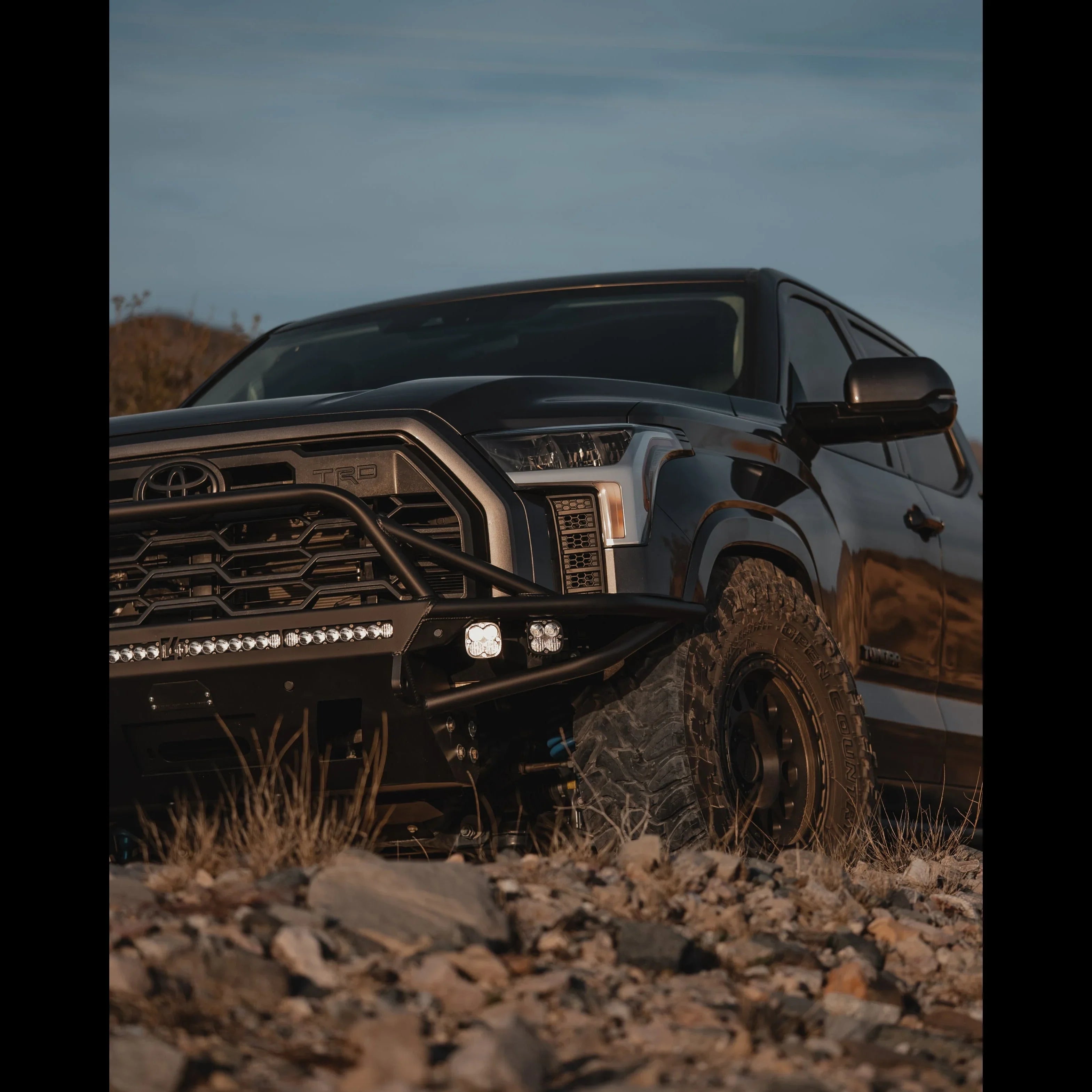 Toyota Tundra with off-road bumper and LED lights parked on rocky terrain at sunset