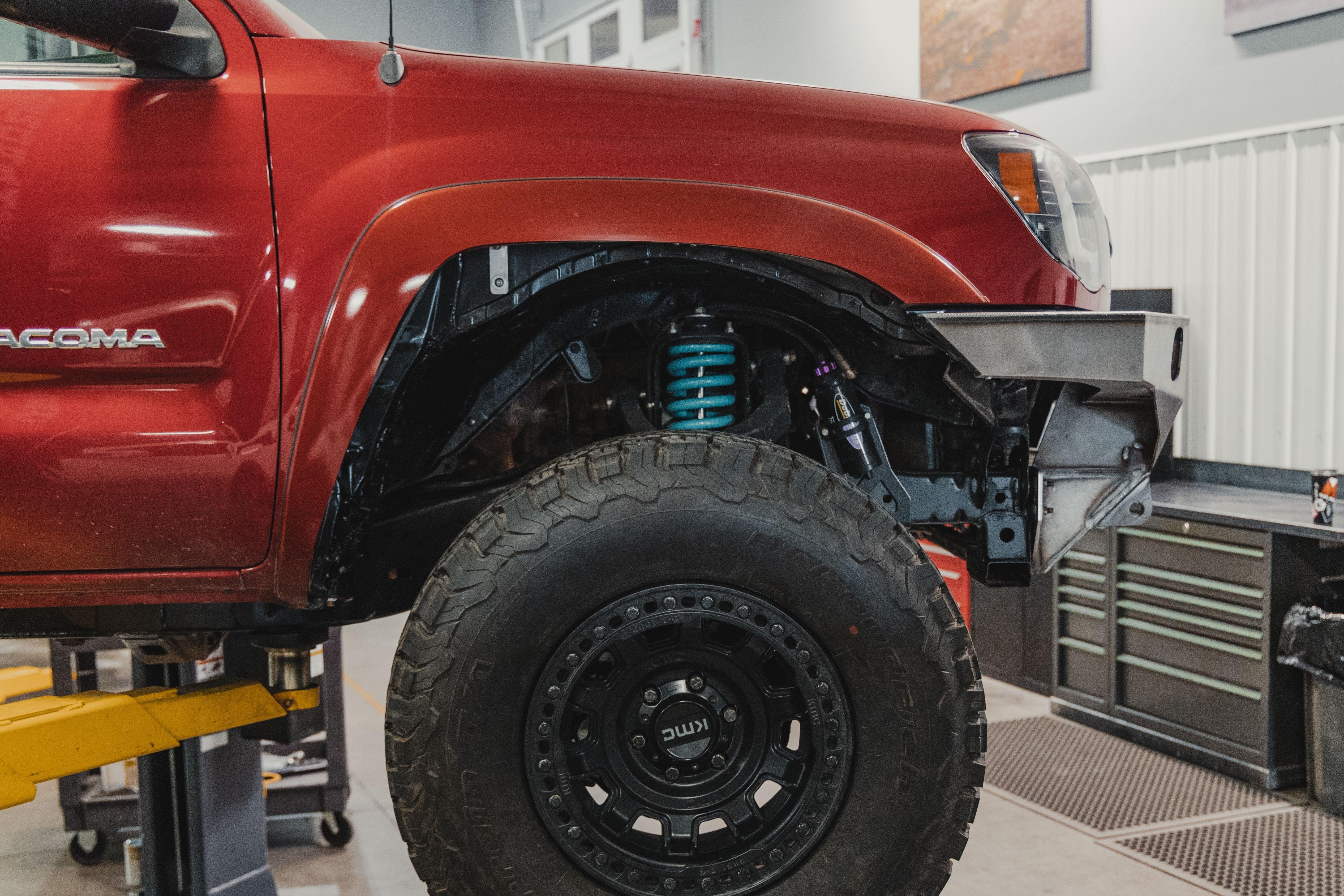 Toyota Tacoma with off-road suspension lift, KMC black wheels, and all-terrain tires in garage