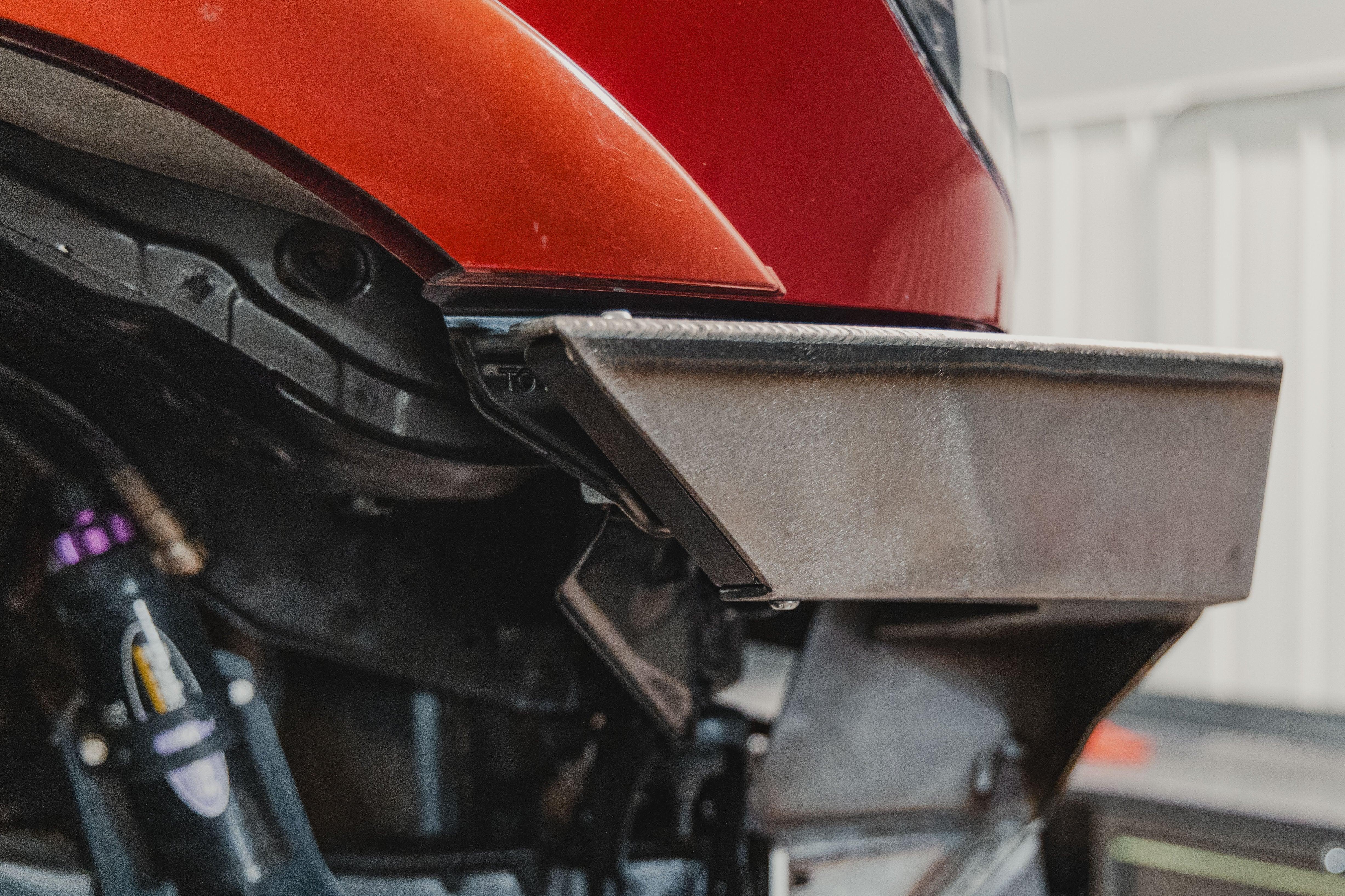 Close-up of a metal off-road bumper corner installed on a red vehicle, showcasing rugged construction.