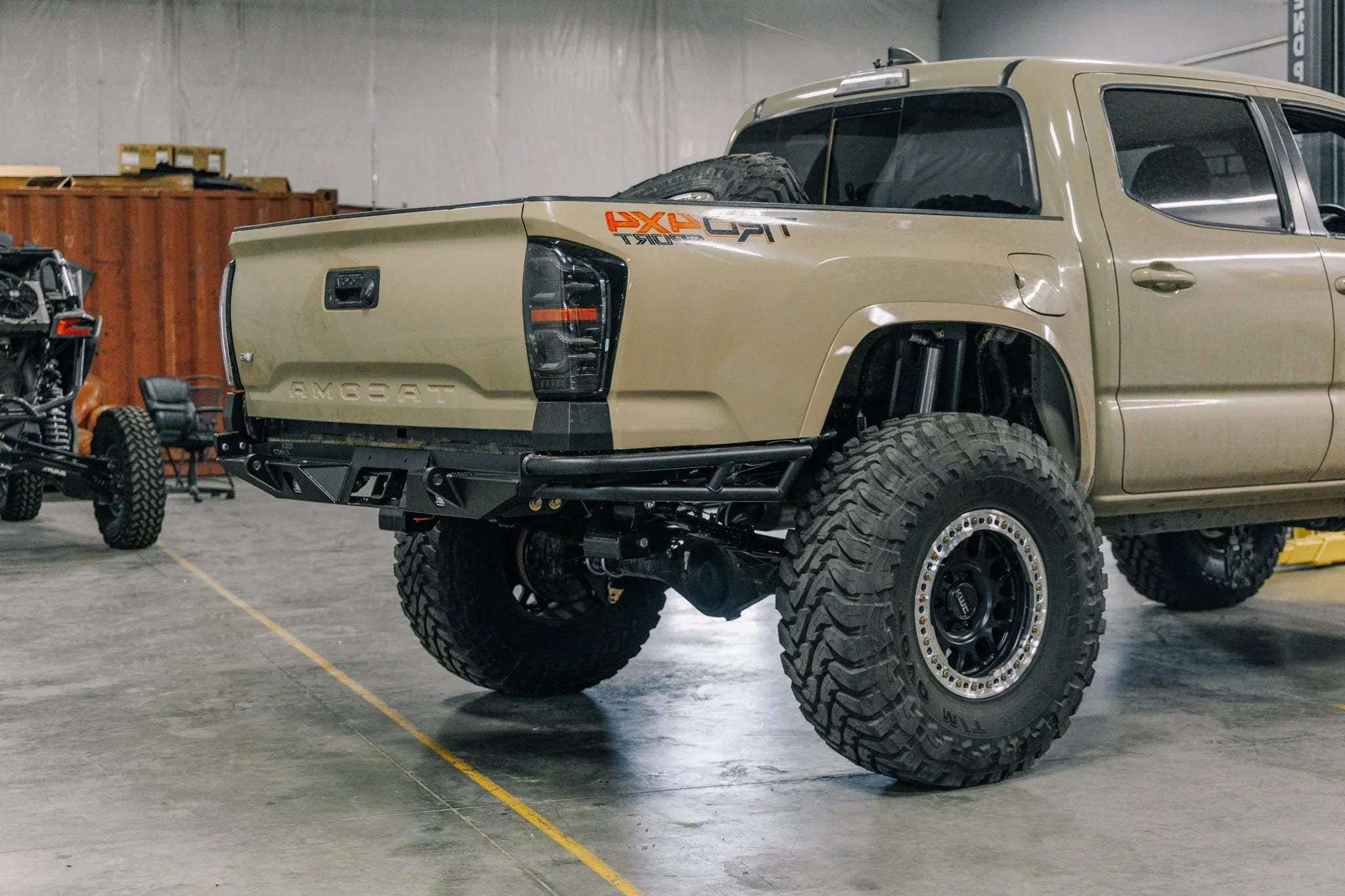 Lifted Toyota Tacoma with off-road tires, black rear bumper, and aftermarket taillights in garage