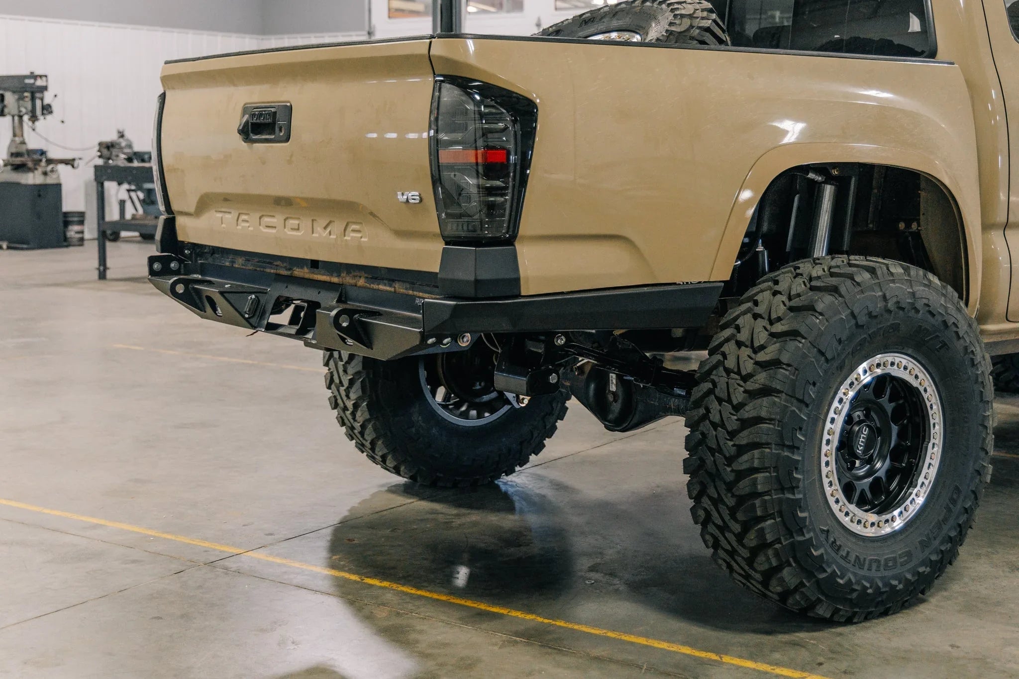 Toyota Tacoma rear with aftermarket off-road bumper and oversized all-terrain tires in garage