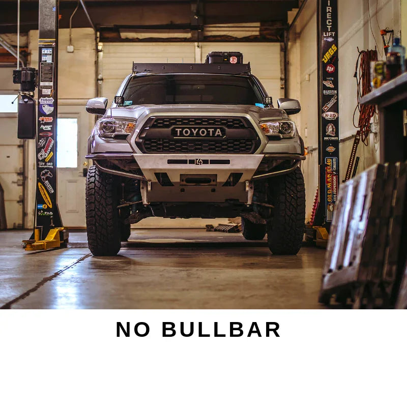 Toyota Tacoma with aftermarket front bumper and off-road accessories in a garage, no bullbar