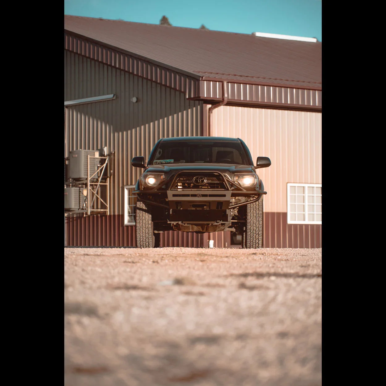Front view Toyota Tacoma truck with off-road bumper parked on gravel near metal building