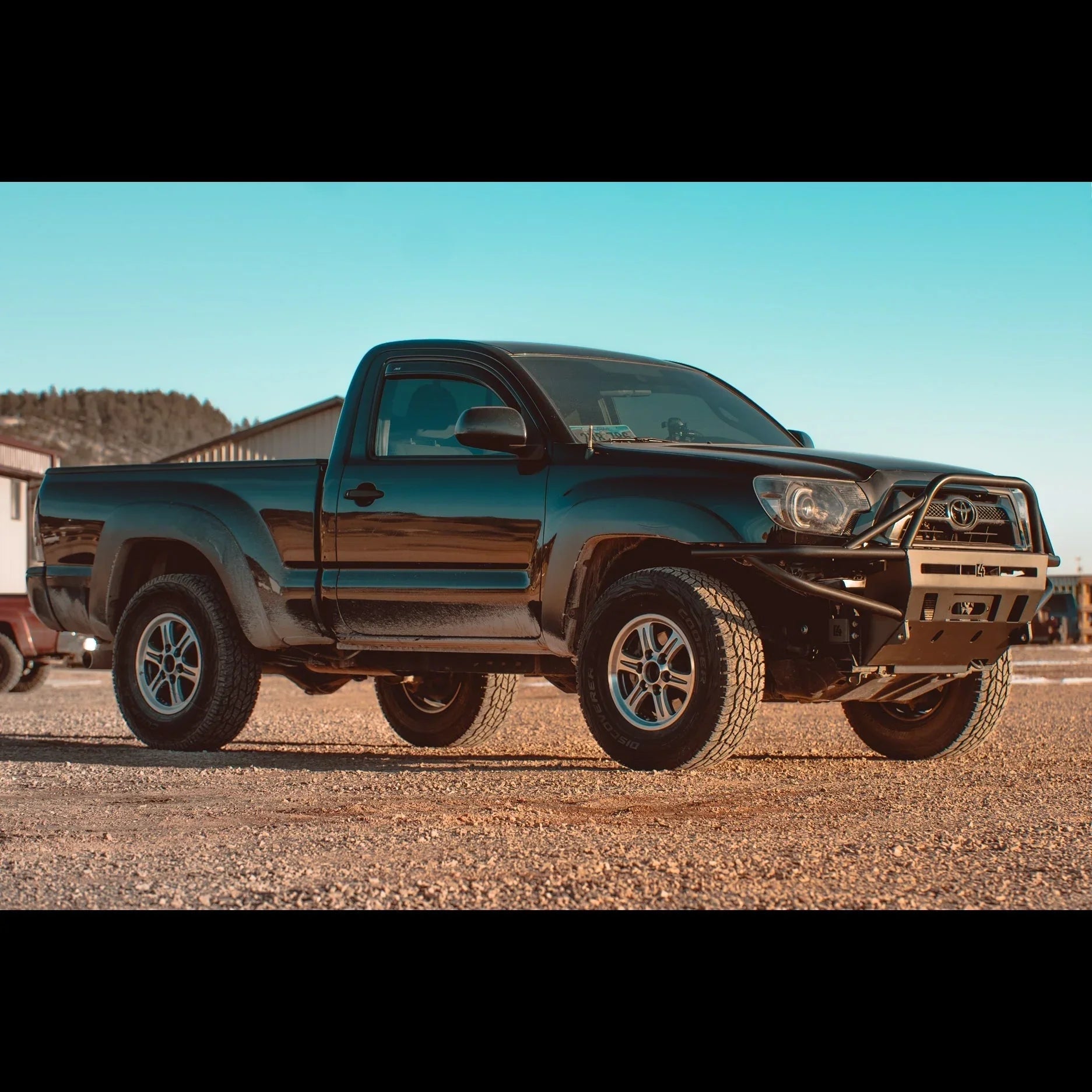 Black Toyota Tacoma with off-road bumper and lift kit parked outdoors on gravel