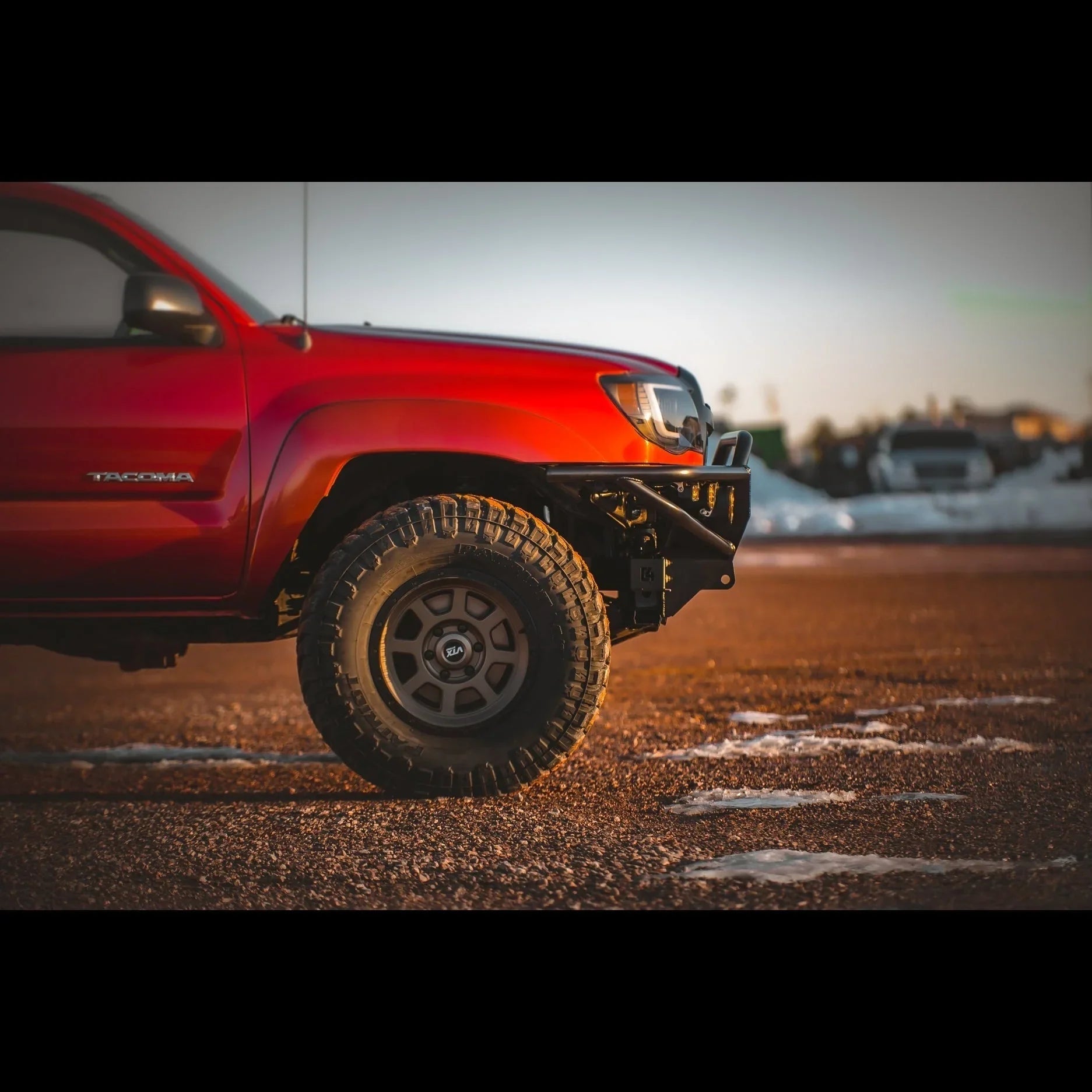 Red Toyota Tacoma with off-road front bumper and rugged all-terrain tire on dirt road