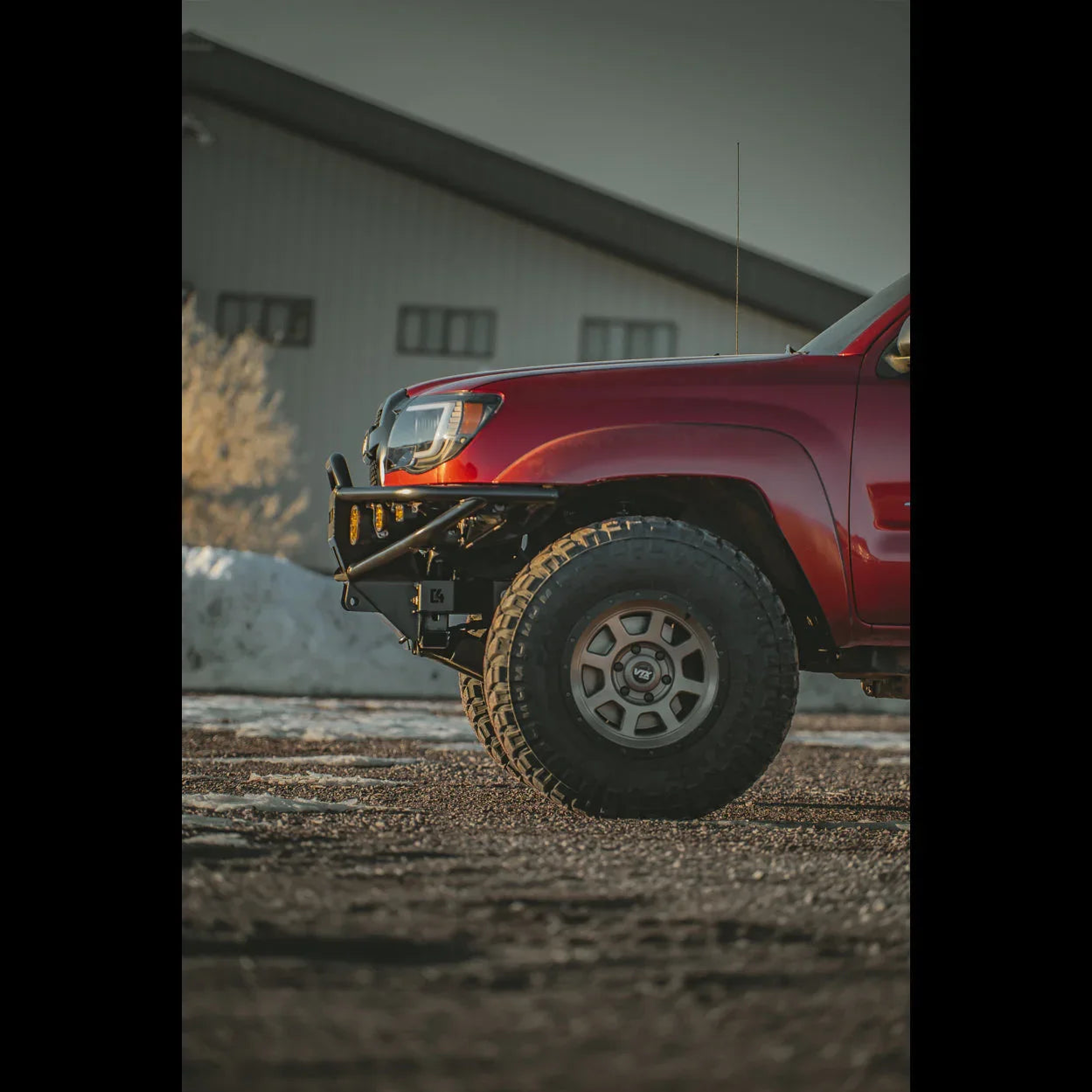 Red Toyota Tacoma with off-road bumper and all-terrain tires, parked outdoors