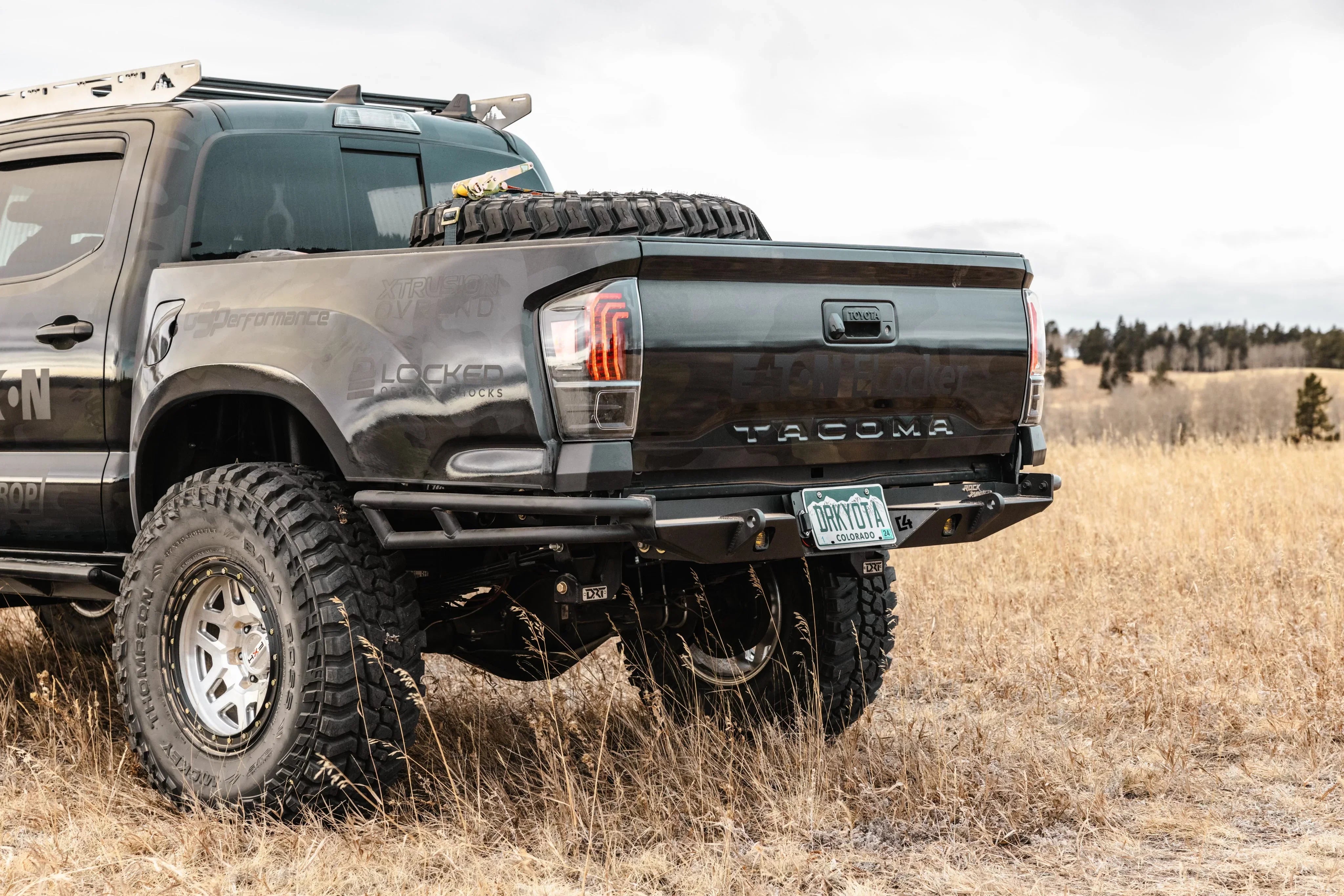 Off-road Toyota Tacoma with aftermarket bumper and spare tire in a grassy field