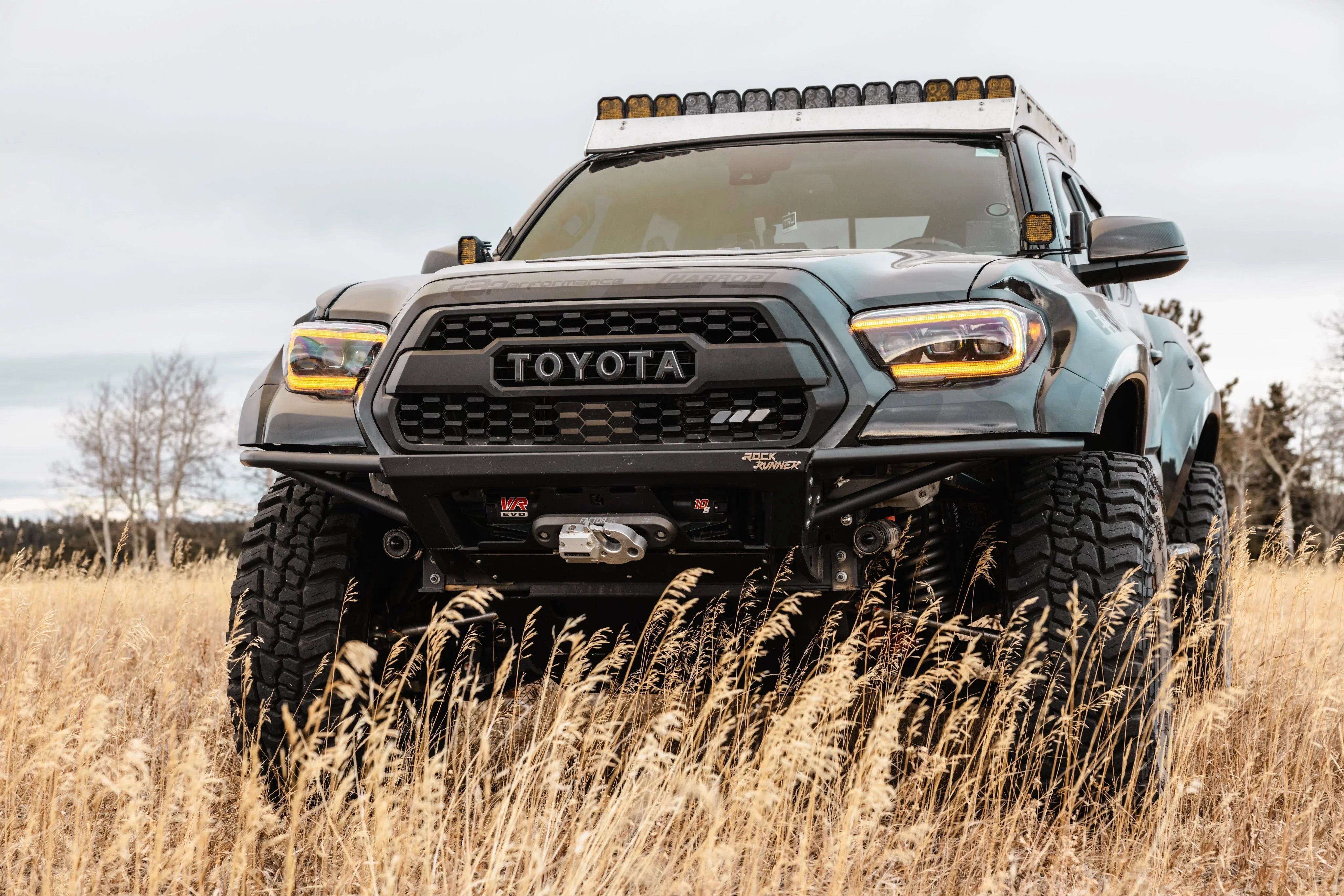 Modified Toyota Tacoma off-road truck with lift kit and roof lights in a grassy field