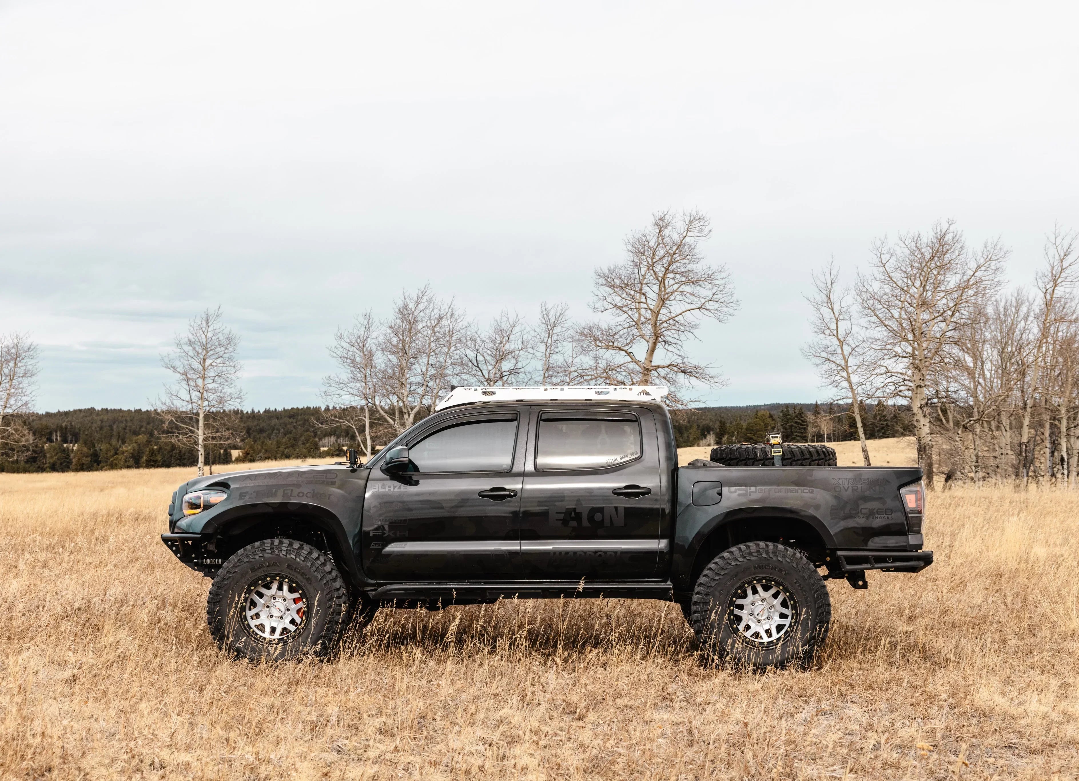 Lifted black Toyota Tacoma overland truck with off-road tires in a grassy field