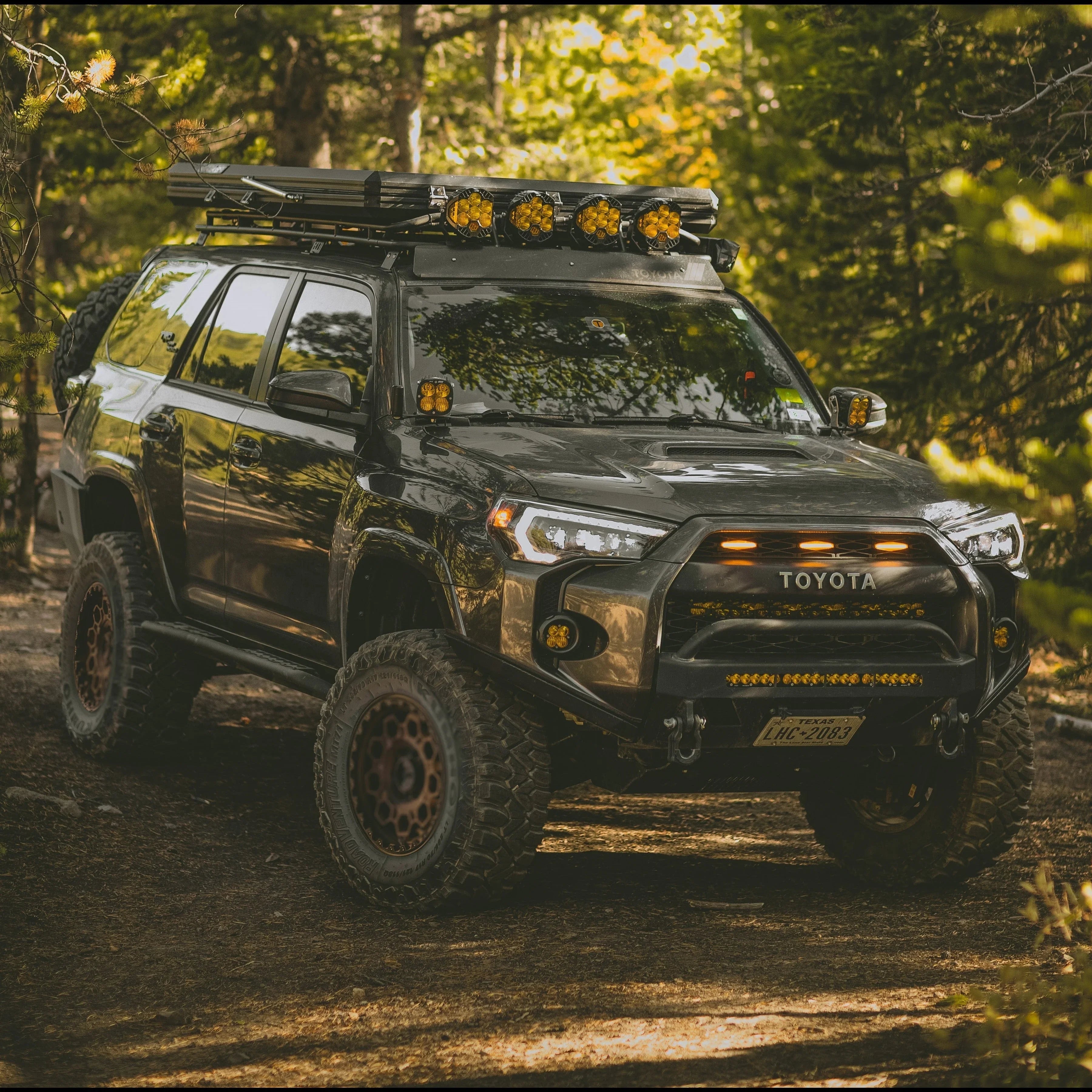 Toyota 4Runner with off-road bumper, roof rack, and lights in a forest trail setting
