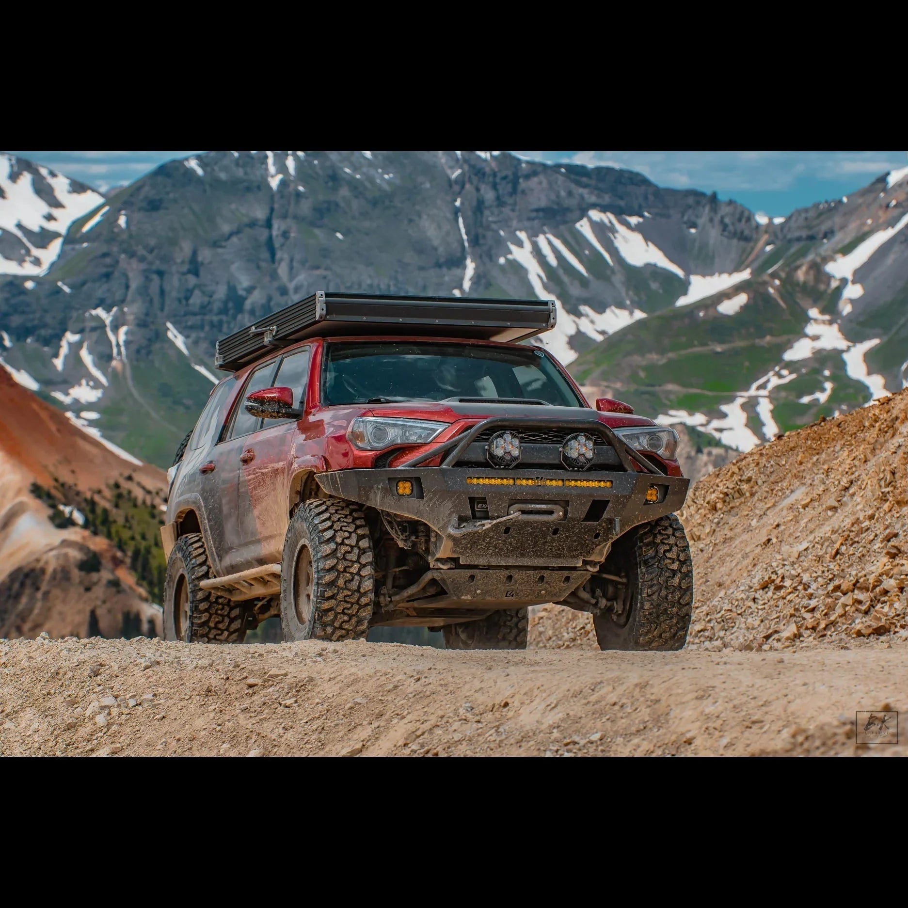 Red Toyota 4Runner with overland front bumper off-road in mountains with snow patches