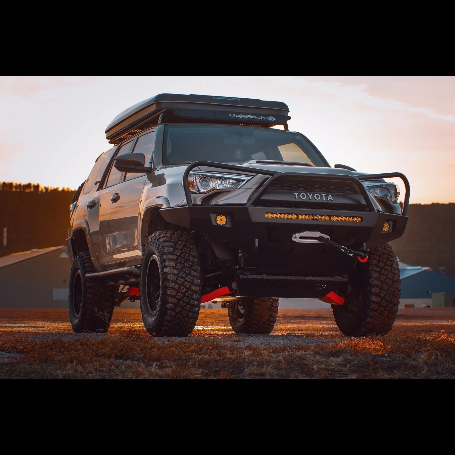 Toyota 4Runner with overland front bumper, winch, roof rack, and off-road tires at sunset