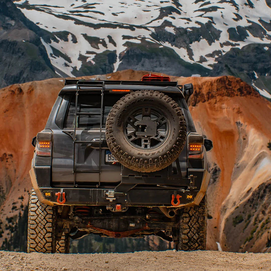 Toyota 4Runner with overlanding rear bumper, spare tire, and off-road gear in mountain terrain