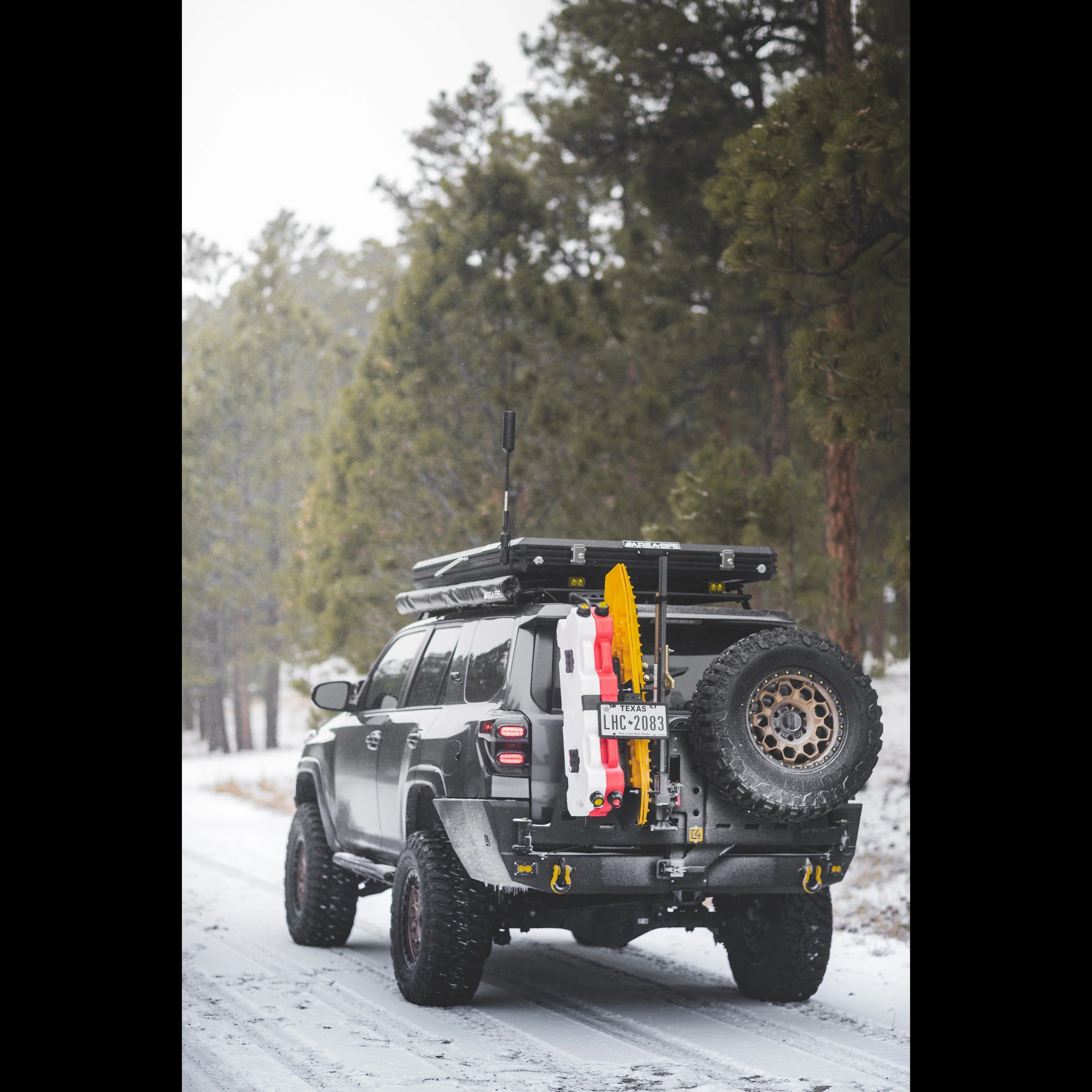 Toyota 4Runner with overland rear bumper, off-road accessories, and spare tire in snowy forest
