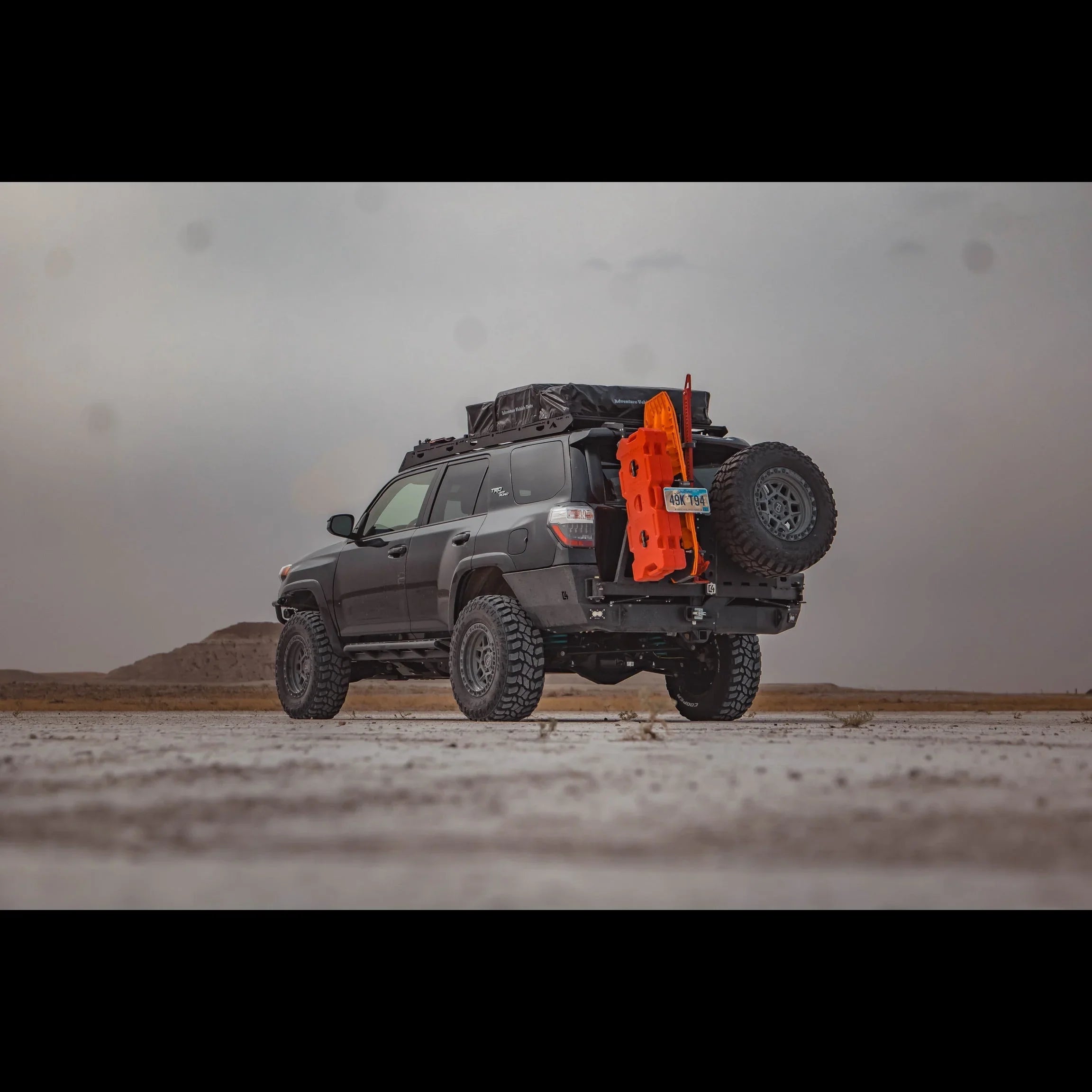 Toyota 4Runner with overland rear bumper, spare tire, recovery boards, and camping gear in desert