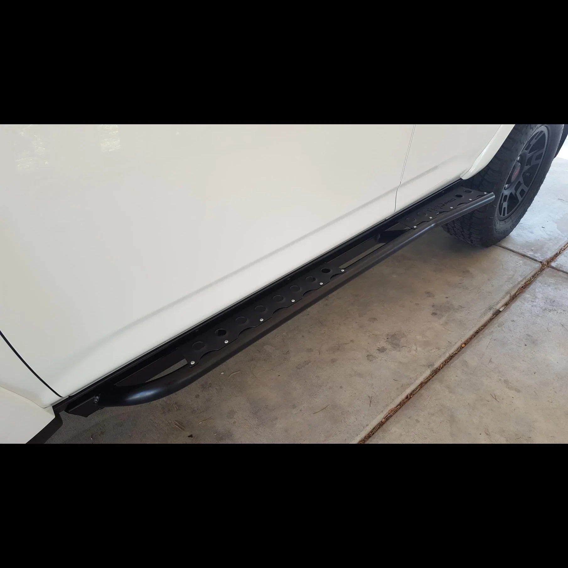 Black rock slider installed on white Toyota 4Runner, 5th Gen, on concrete driveway