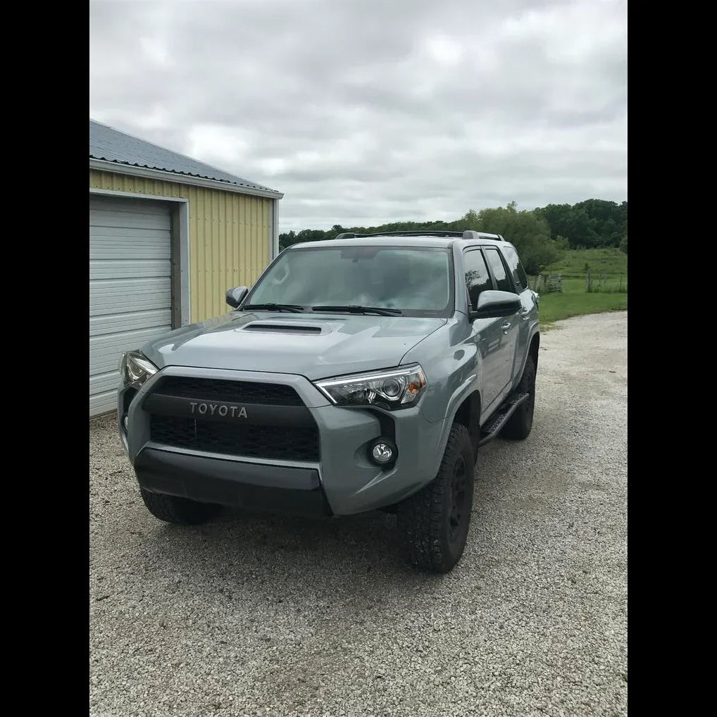 Gray Toyota 4Runner 5th Gen with rock sliders parked on gravel by a garage