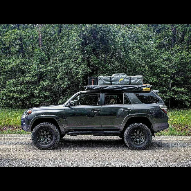 Toyota 4Runner with roof rack, tent, camping gear and rock sliders in a forest setting