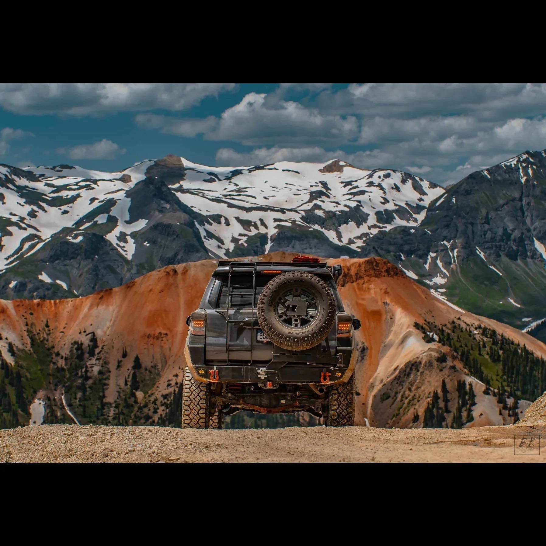 Toyota 4Runner with rear hatch ladder and spare tire on mountain trail, snowy peaks in background