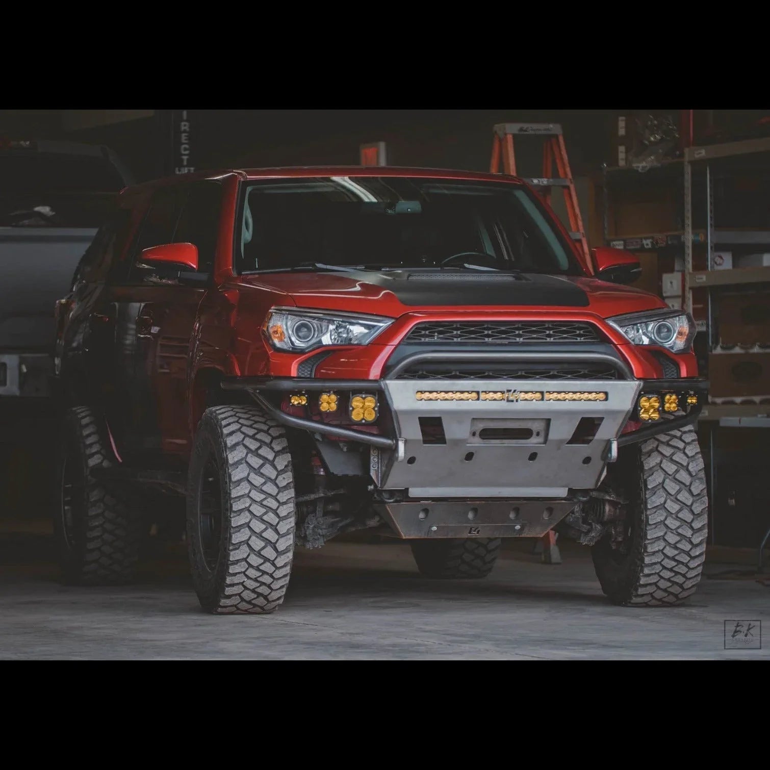 Red Toyota 4Runner with off-road bumper, LED lights, and all-terrain tires in garage
