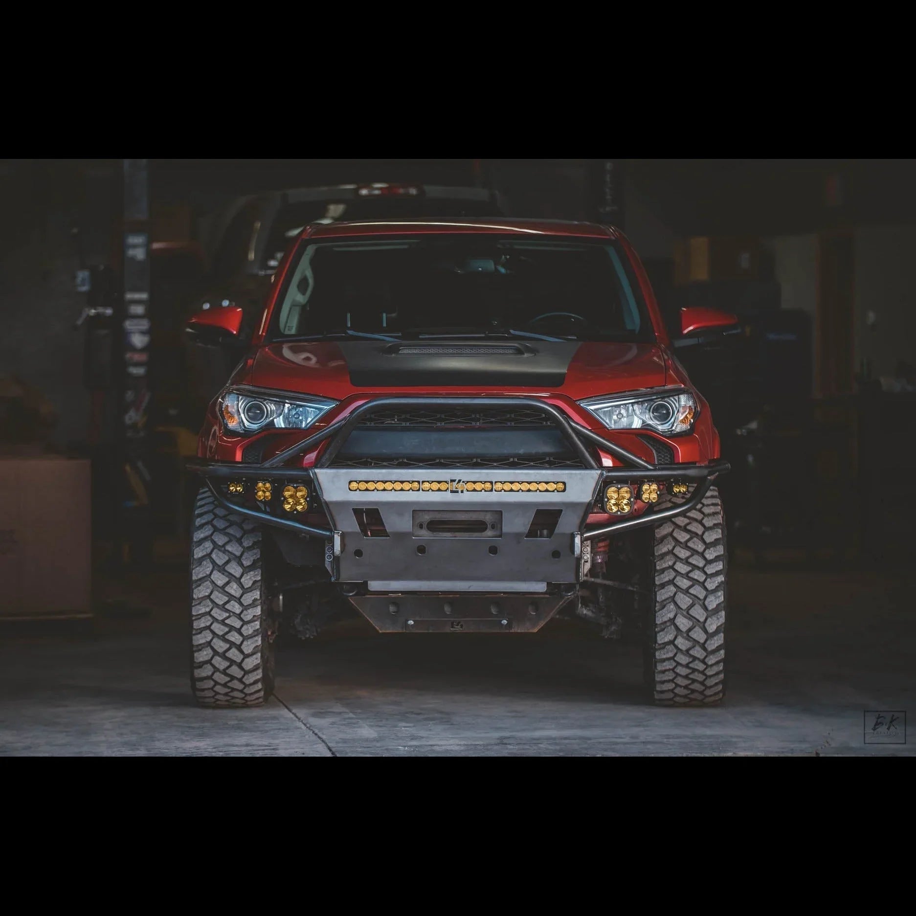 Red Toyota 4Runner with off-road front bumper, LED lights, and all-terrain tires in a garage