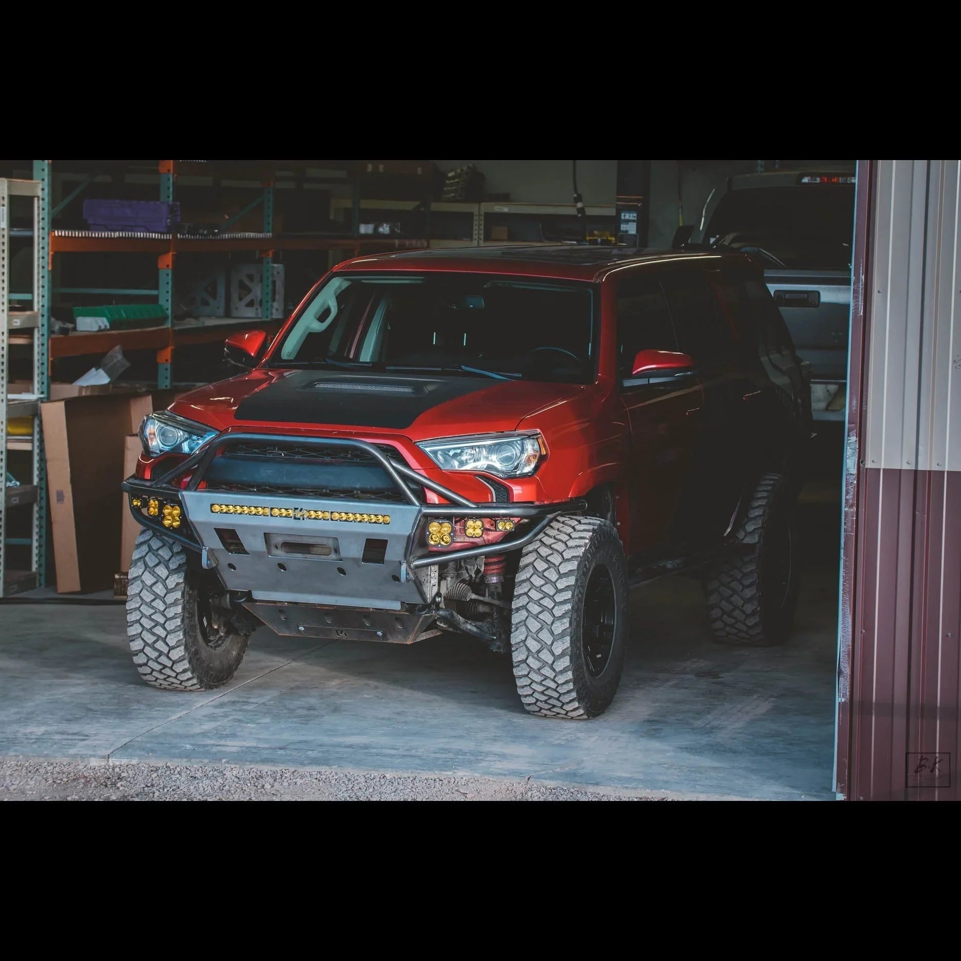 Red Toyota 4Runner with off-road tires and aftermarket front bumper in a garage