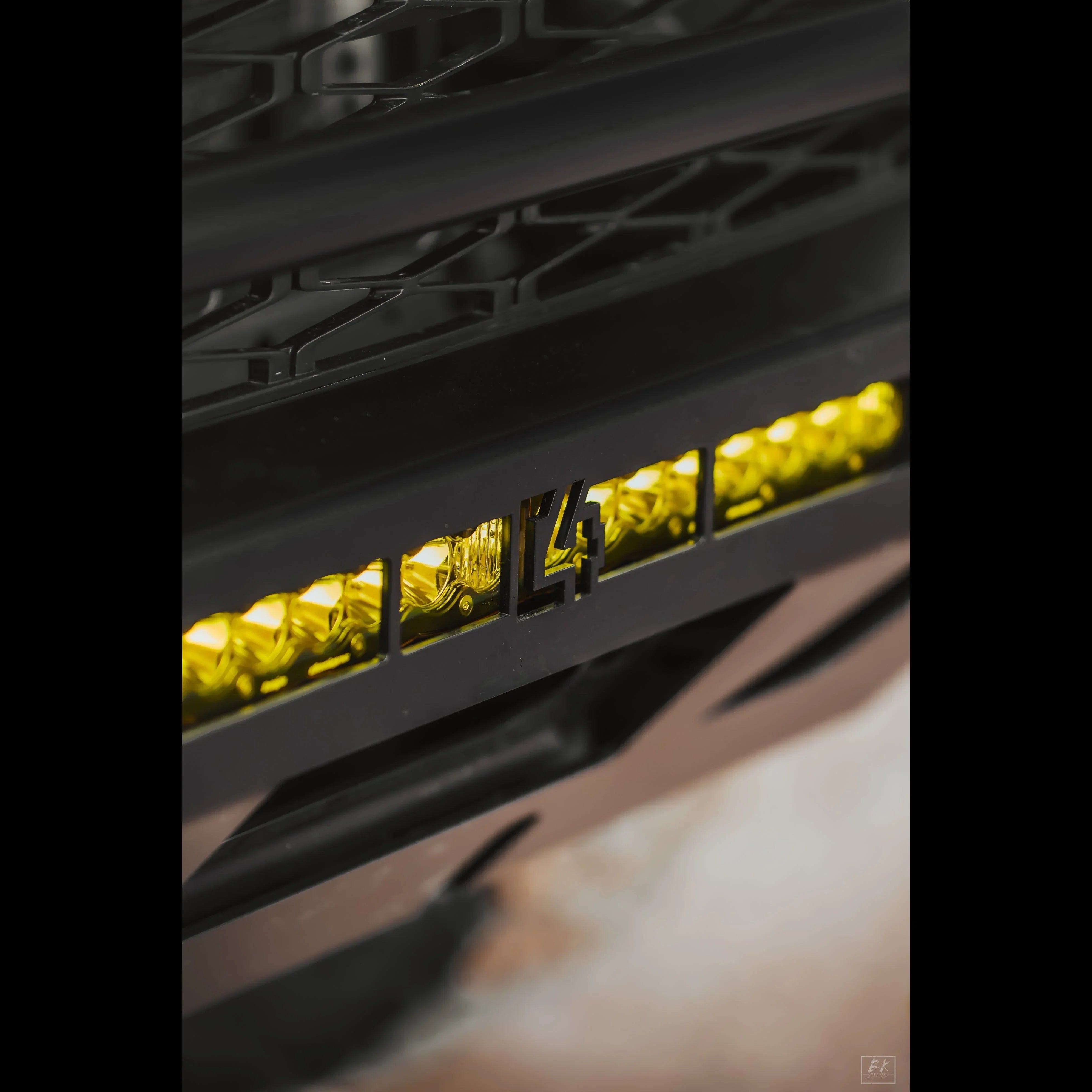 Close-up of off-road vehicle bumper with LED amber light bar and metal grille insert.