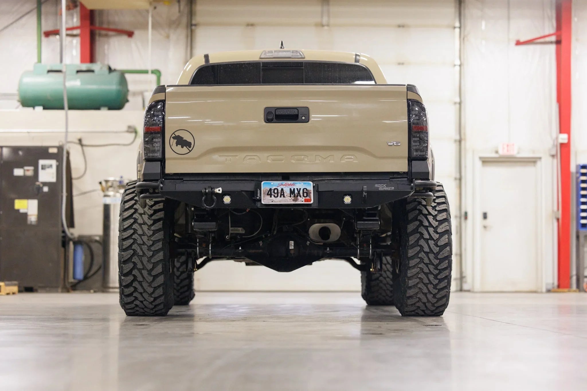 Lifted Toyota Tacoma rear view with off-road tires and black aftermarket bumper in a garage