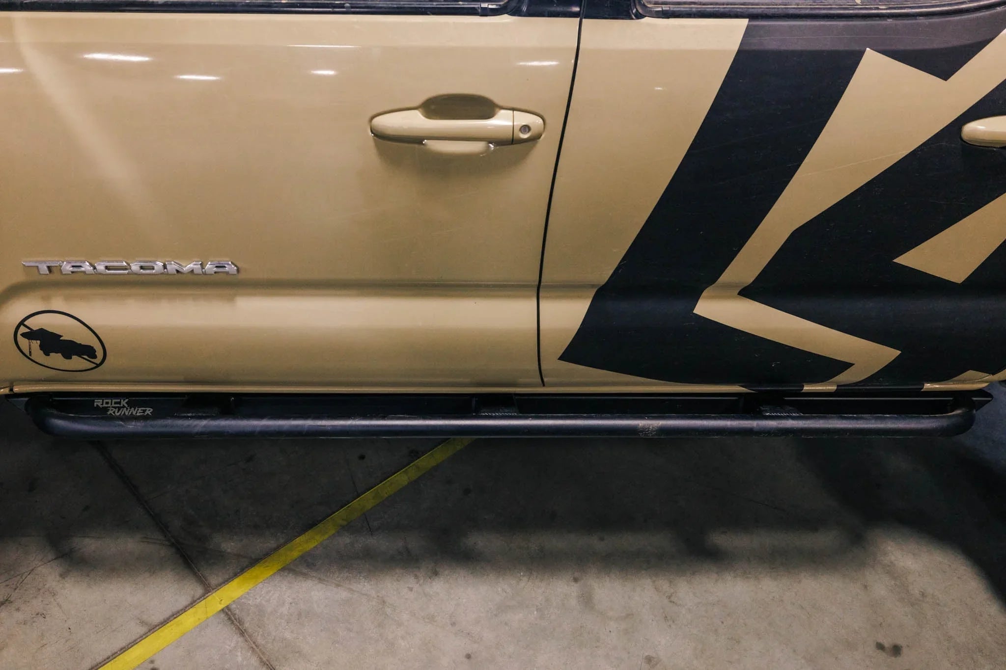 Closeup of a Toyota Tacoma side door with Rock Runner rock slider and off-road decal