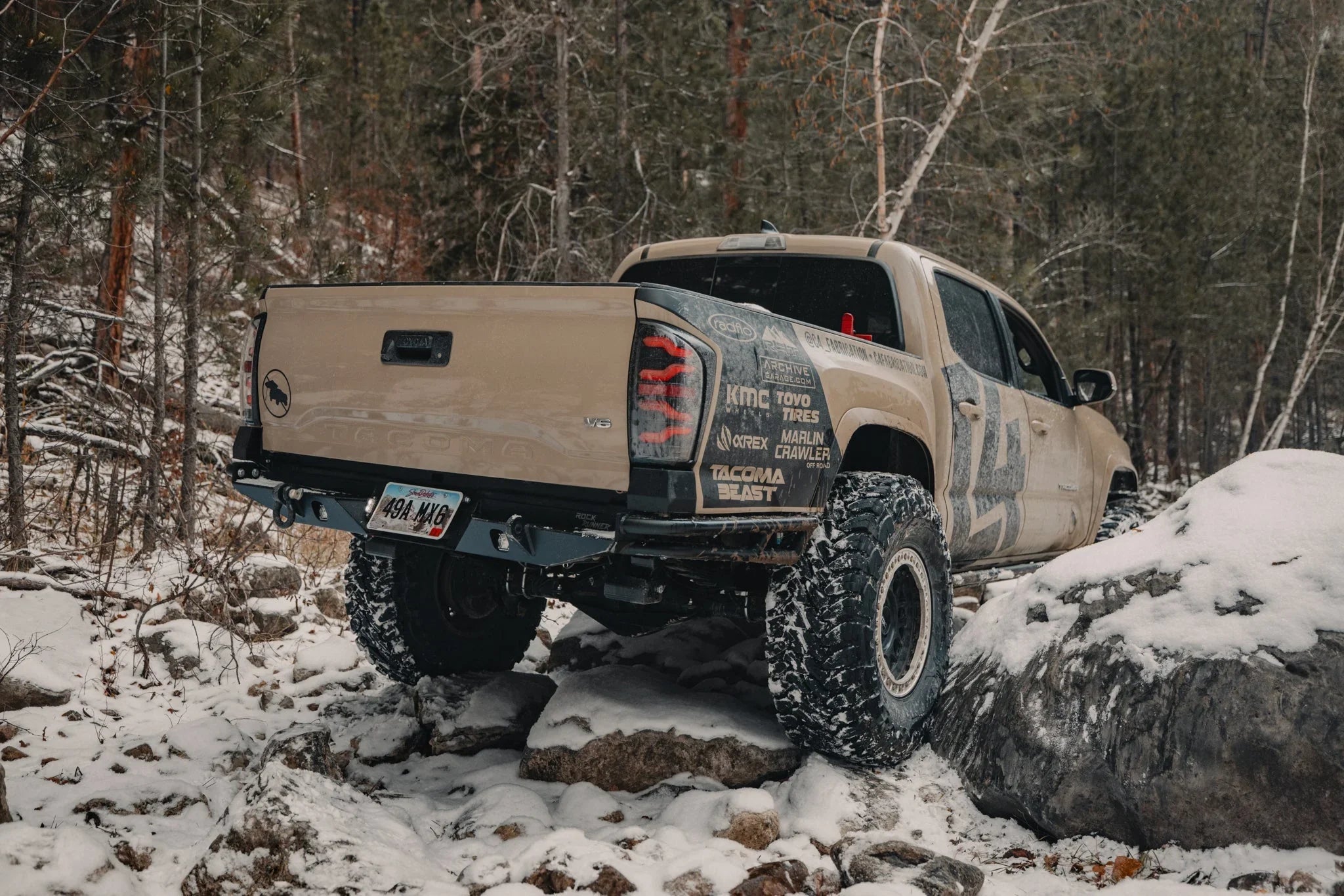 Toyota Tacoma off-road truck with all-terrain tires rock crawling in snowy forest