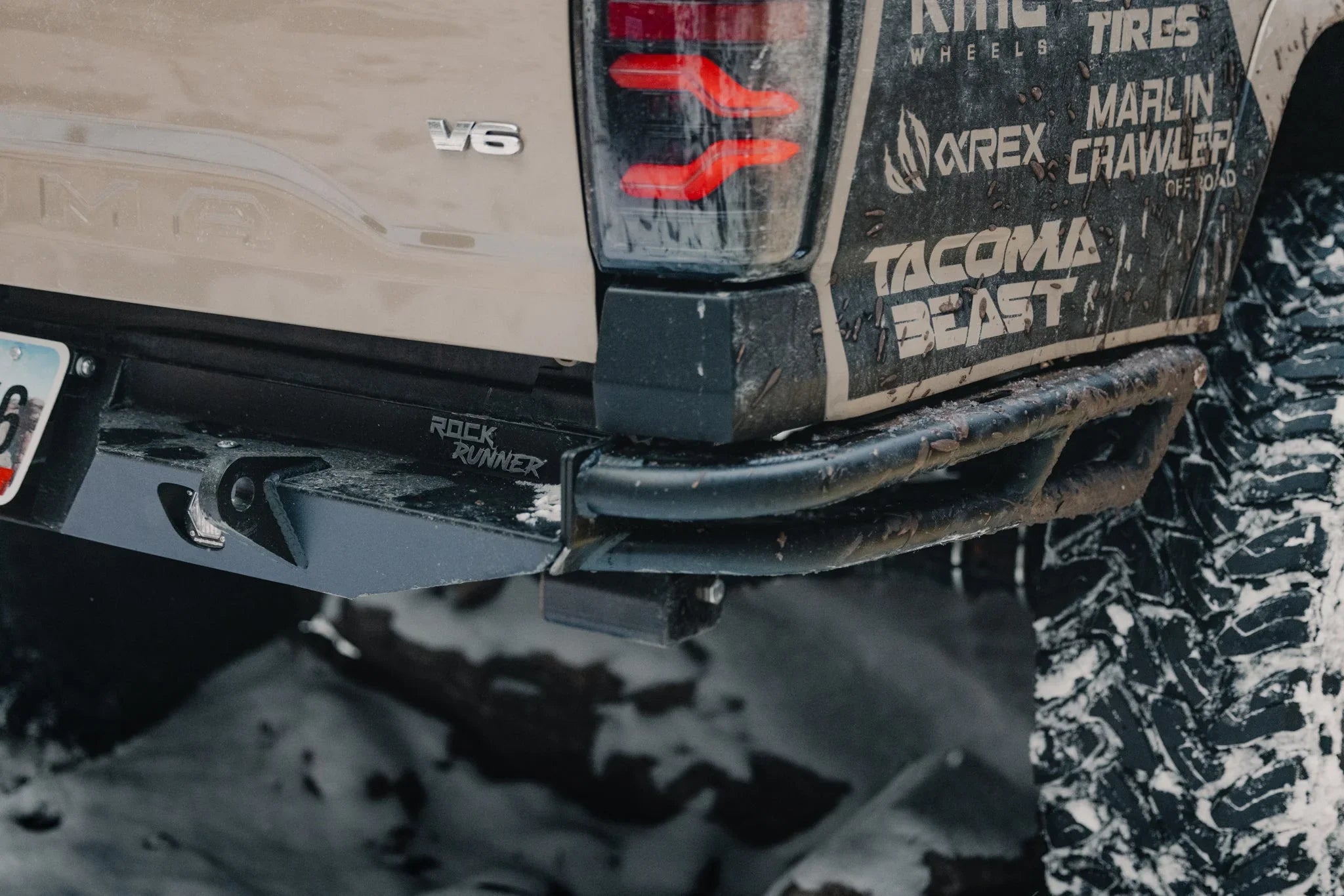 Toyota Tacoma rear with off-road bumper, mud-covered decals, and rugged all-terrain tire