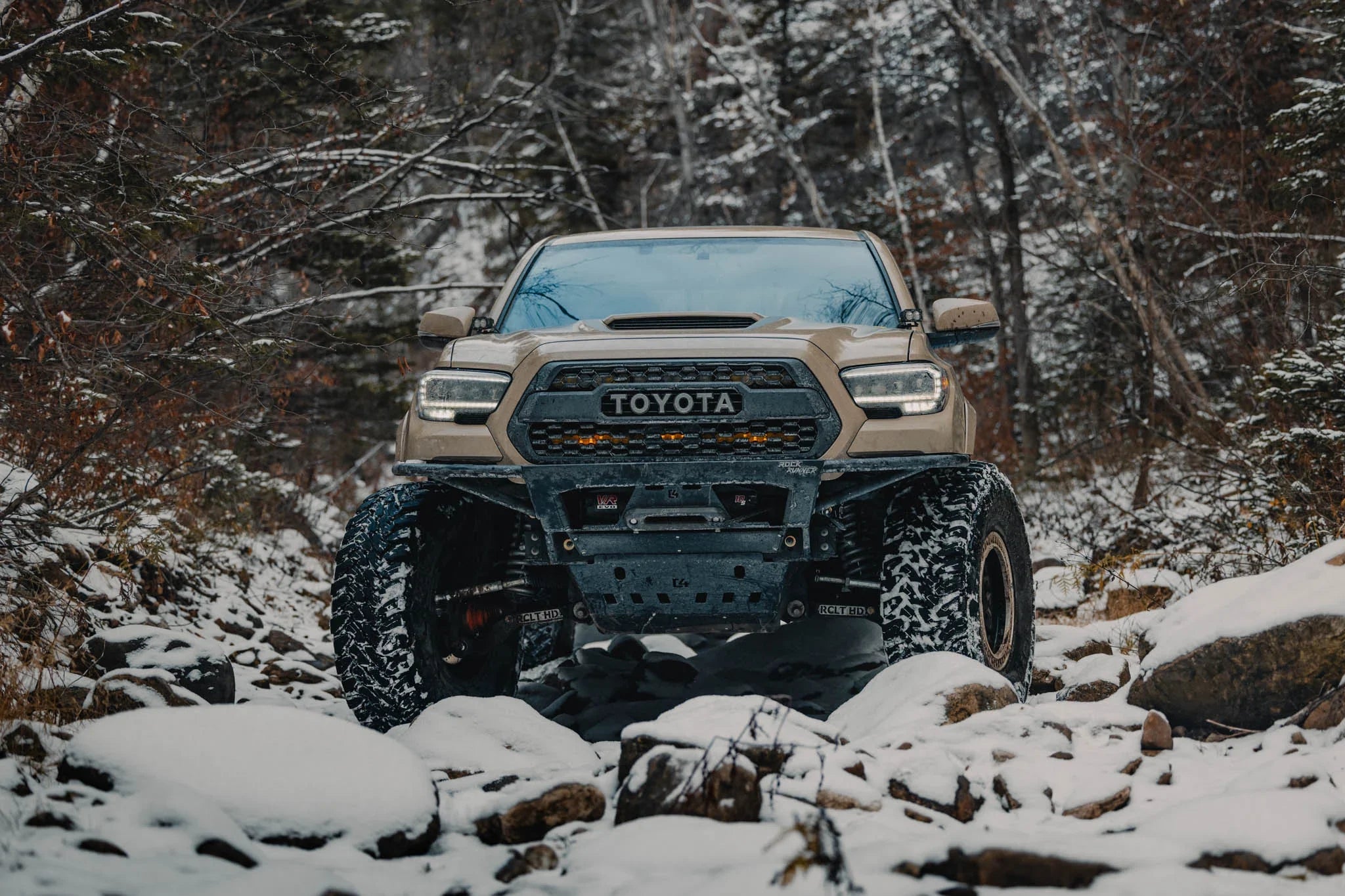 Toyota Tacoma off-road truck with rugged tires on snowy, rocky trail in winter forest