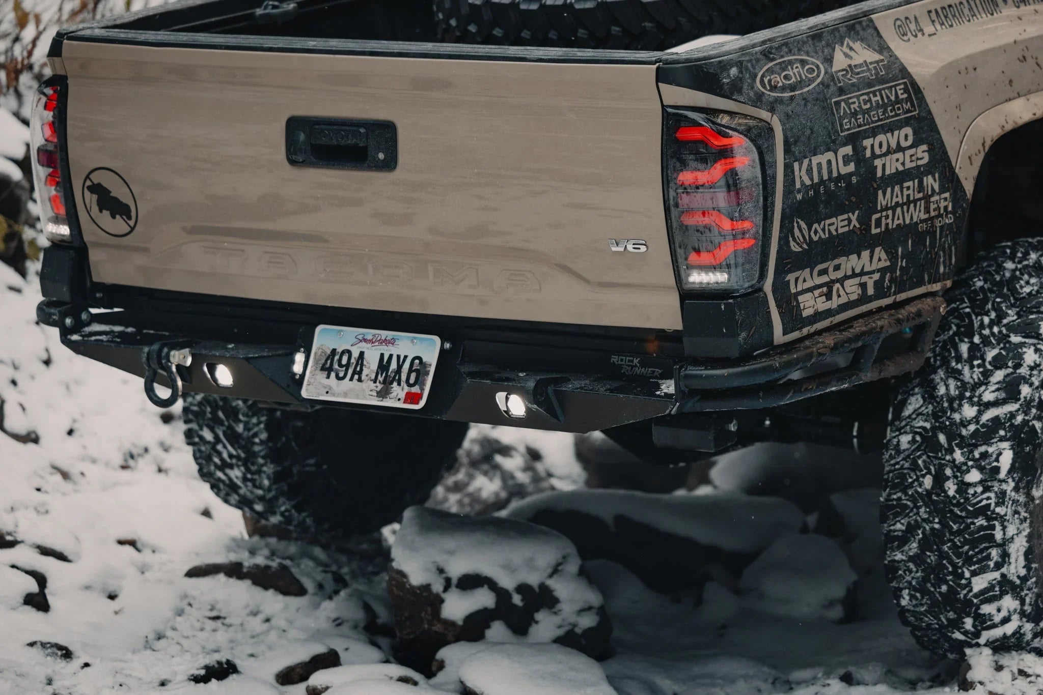 Toyota Tacoma rear with off-road bumper, mud-terrain tires, decals, snow-covered trail