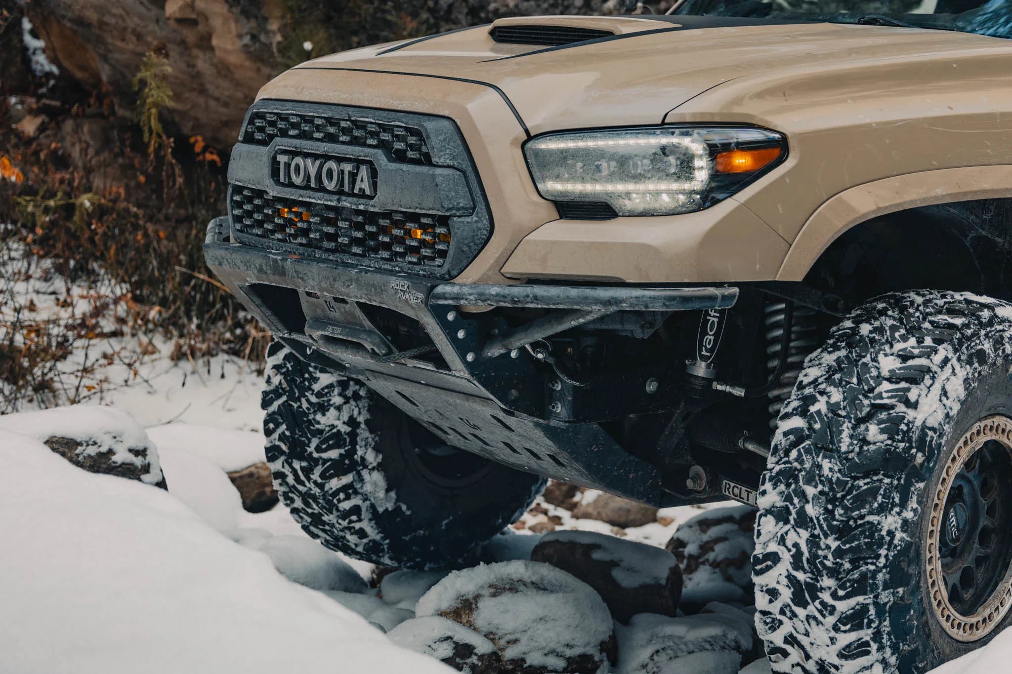 Off-road Toyota Tacoma with lifted suspension and rugged tires driving in snowy terrain