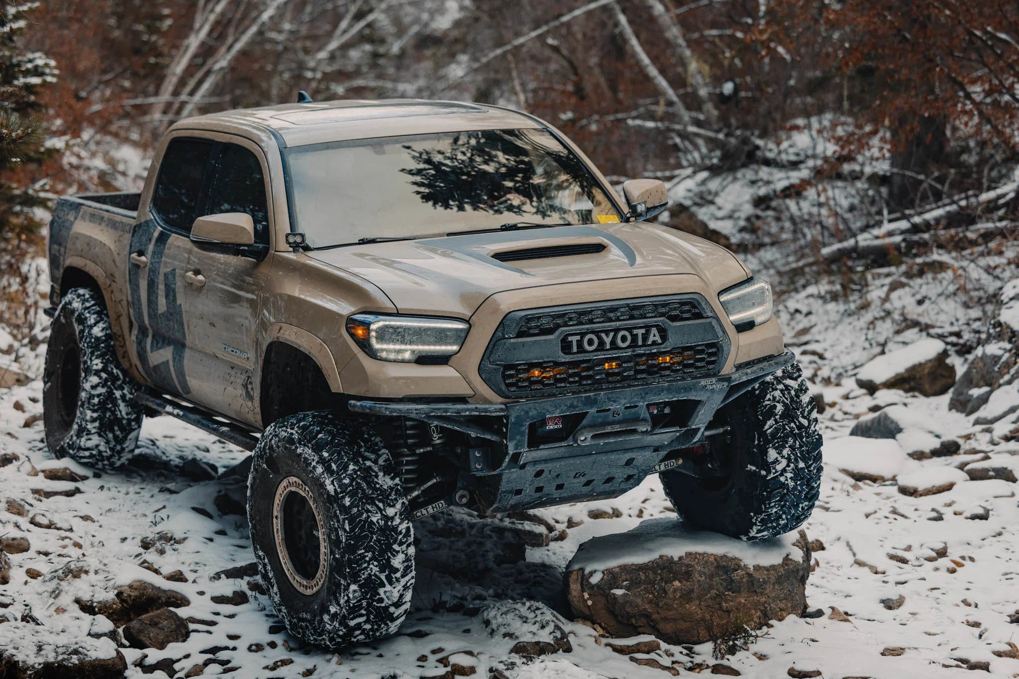 Lifted Toyota Tacoma off-road truck with mud tires in a snowy forest trail