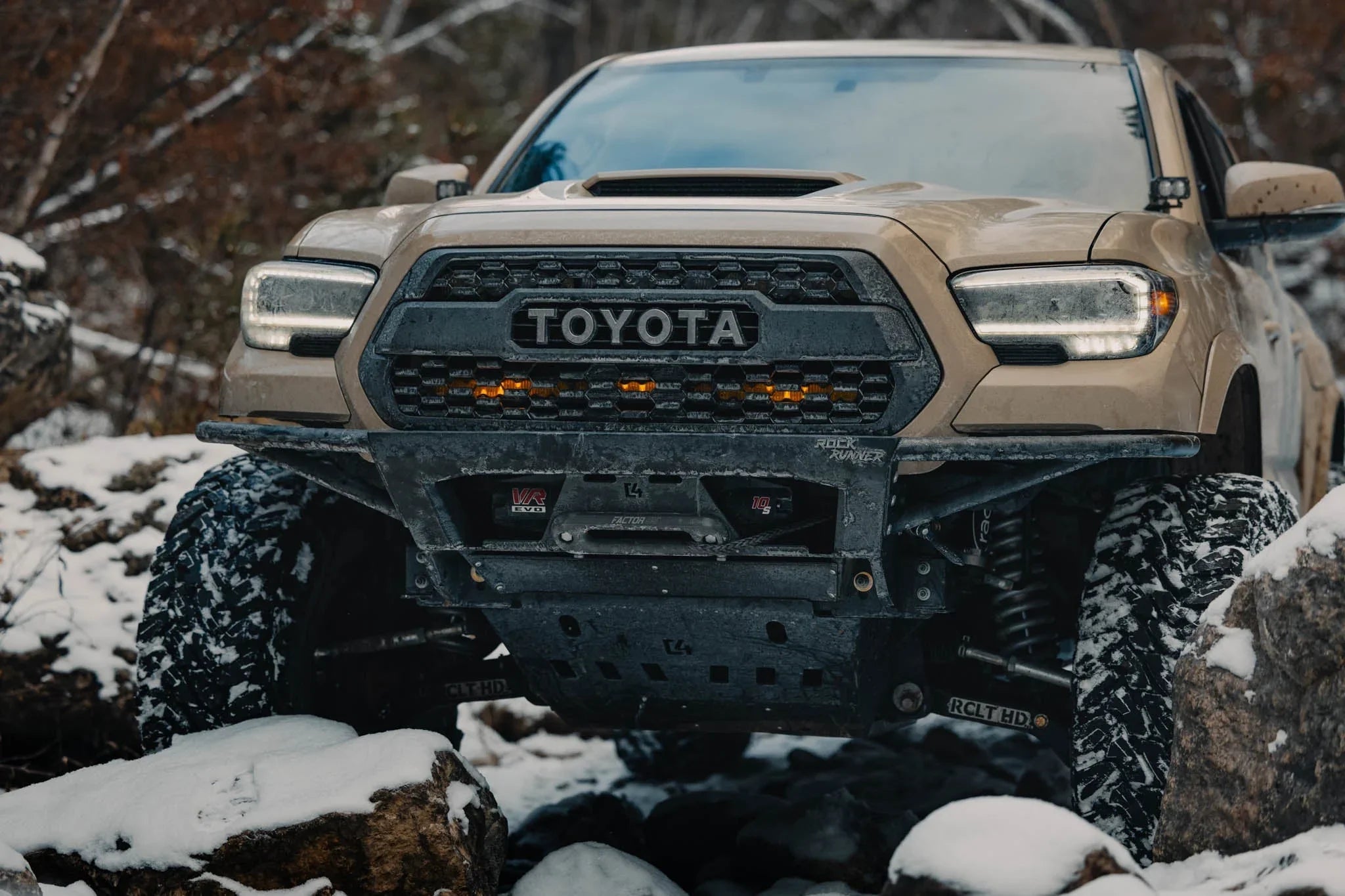 Toyota Tacoma with off-road bumper and snow-covered tires on a rocky winter trail