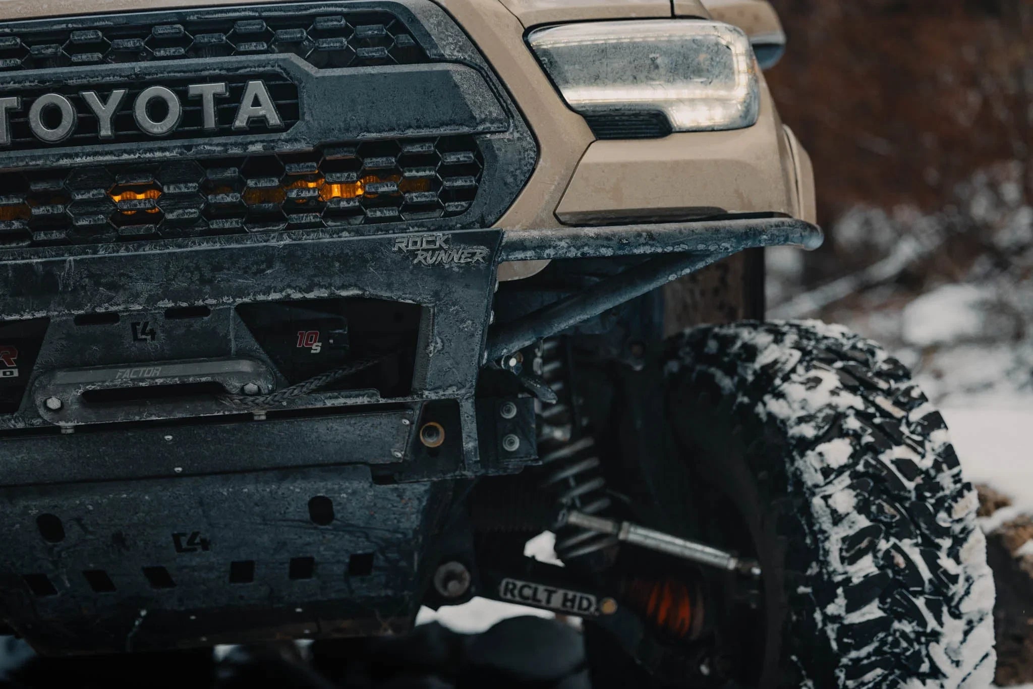 Toyota Tacoma front end with off-road bumper, snow-covered tire, and Rock Runner skid plate