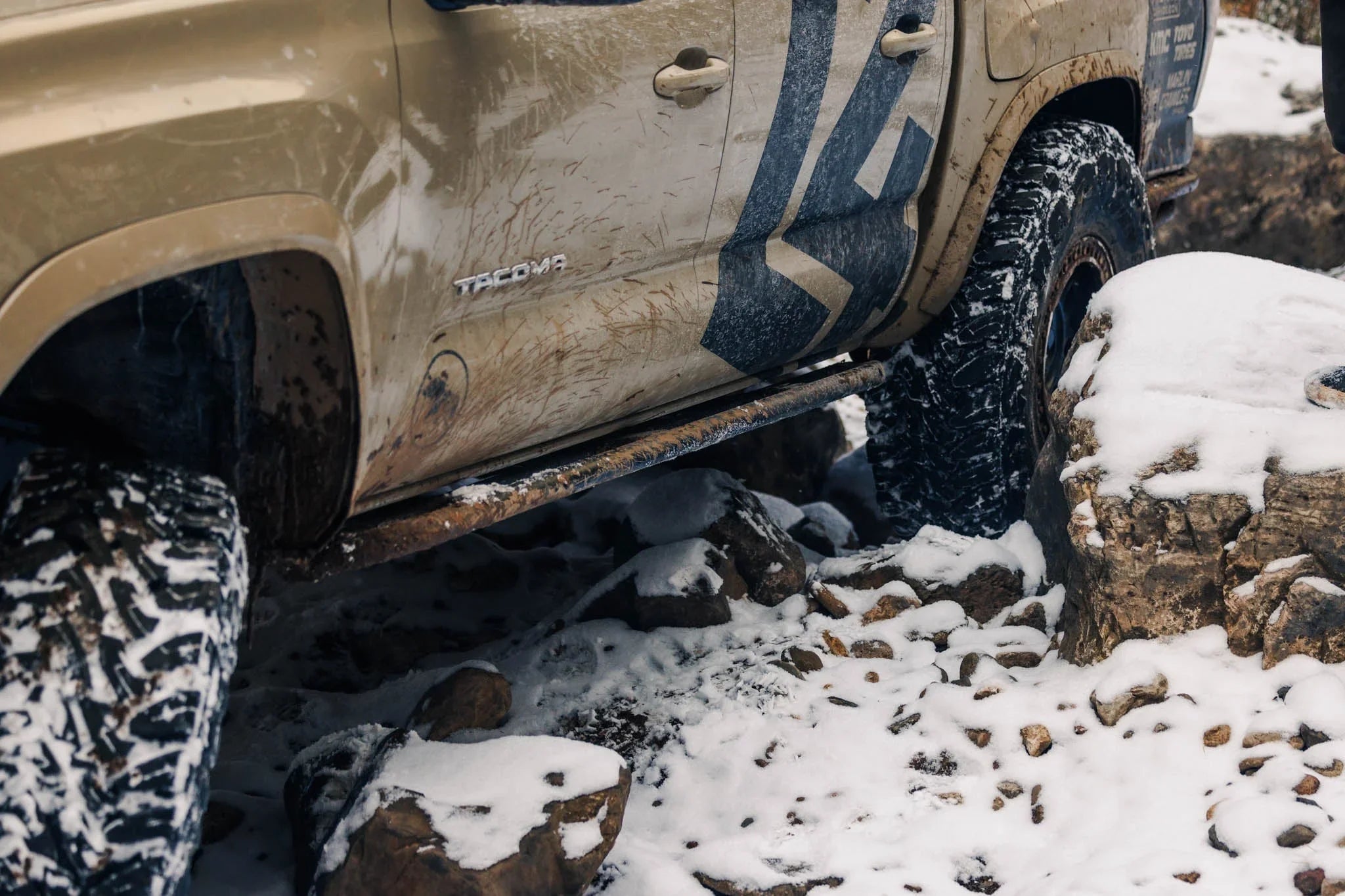 Toyota Tacoma off-road truck with mud and snow tires climbing snowy rocks