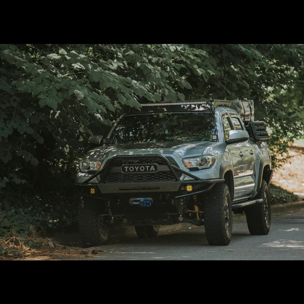 Toyota Tacoma overland truck with off-road accessories parked by forest edge