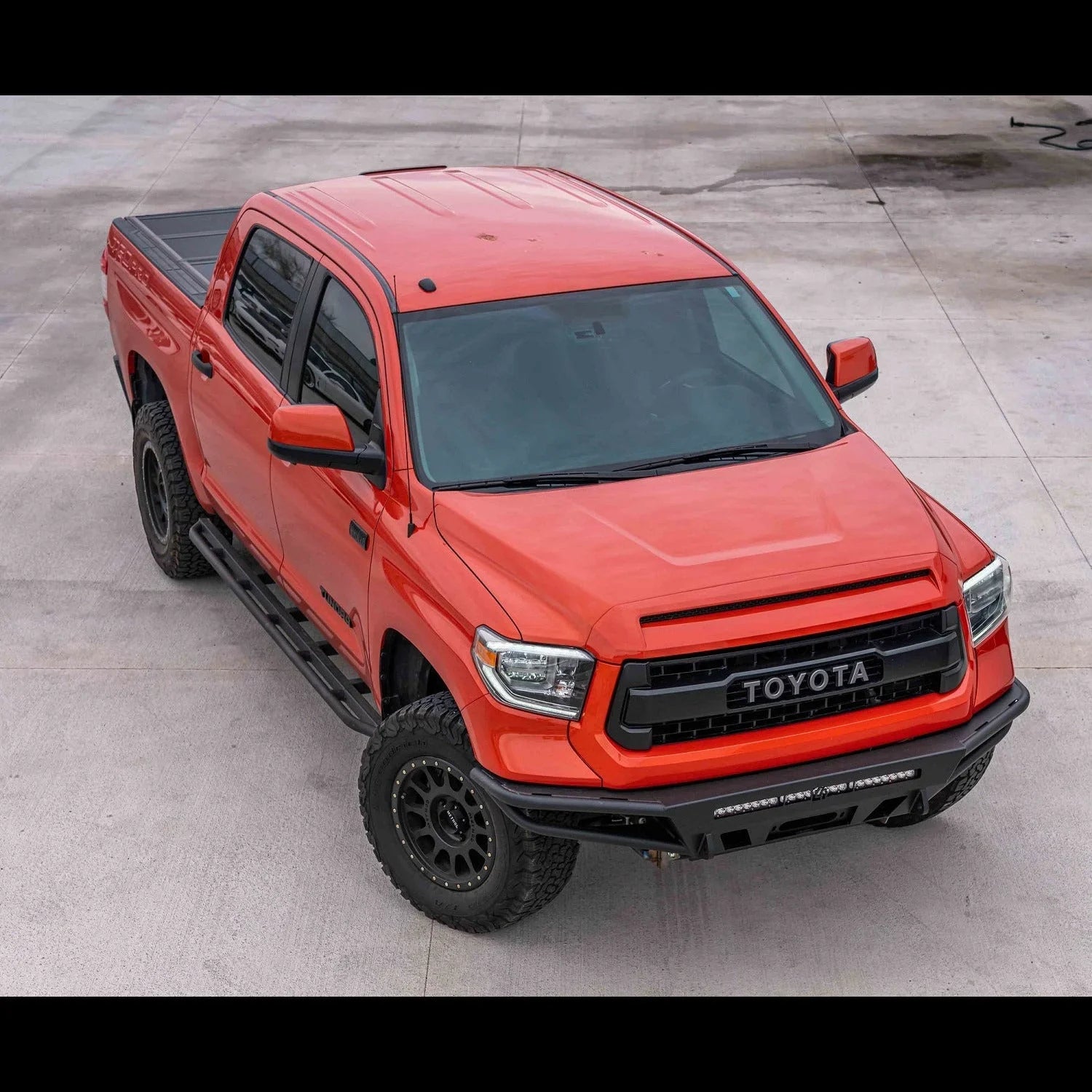 Red Toyota Tundra with off-road tires and aftermarket front bumper on concrete