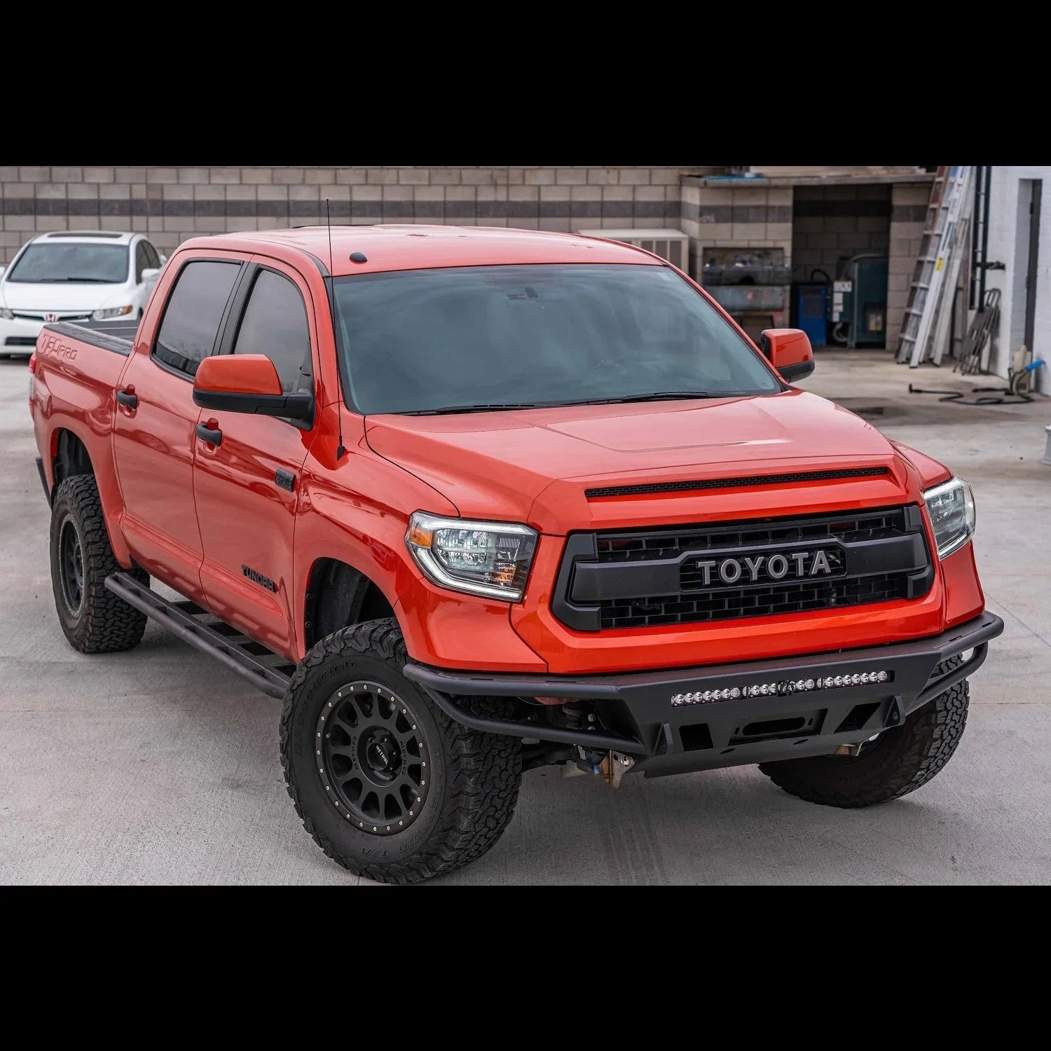 Red Toyota Tundra pickup with off-road front bumper, LED light bar, black wheels, side steps