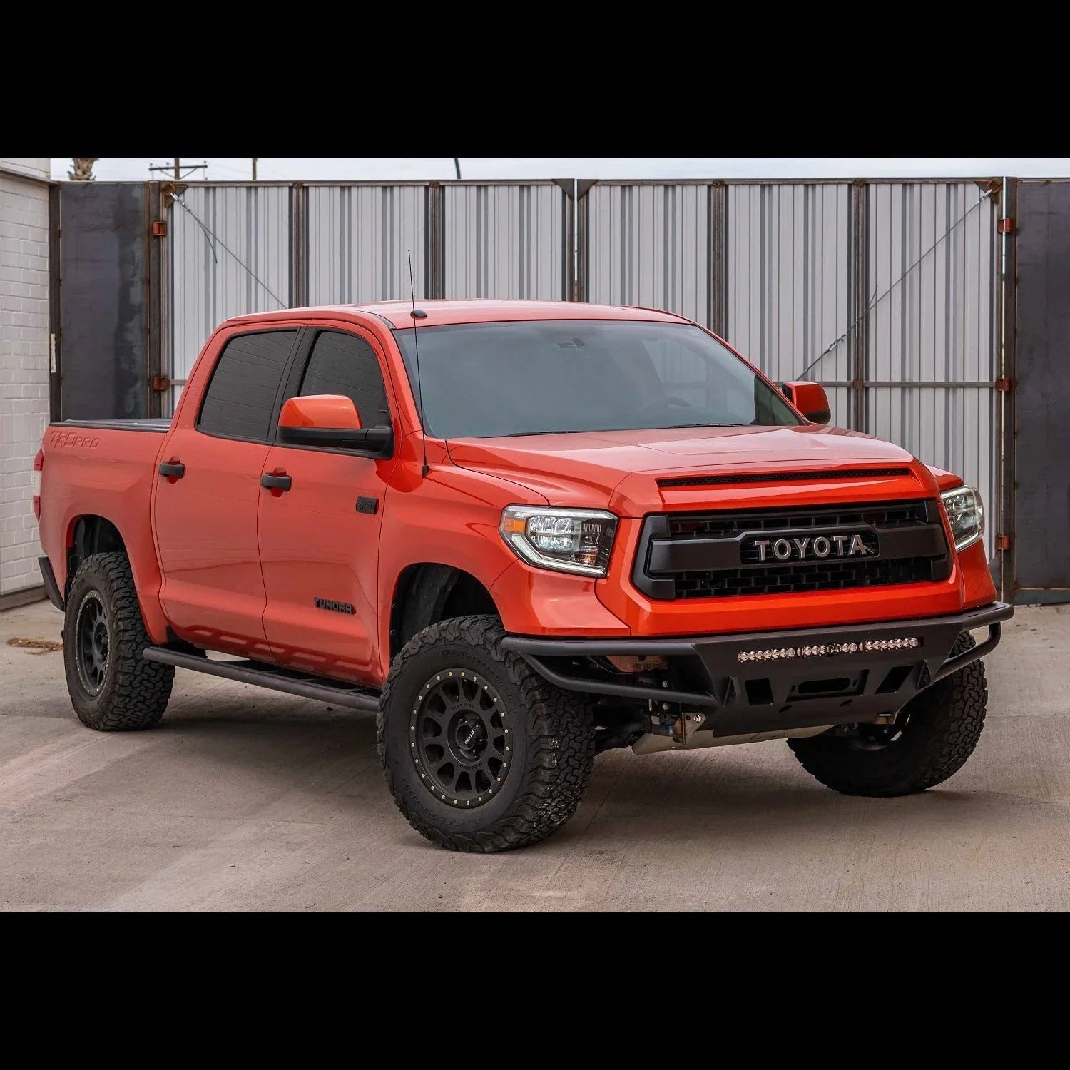 Lifted orange Toyota Tundra truck with off-road tires and steel front bumper in urban setting