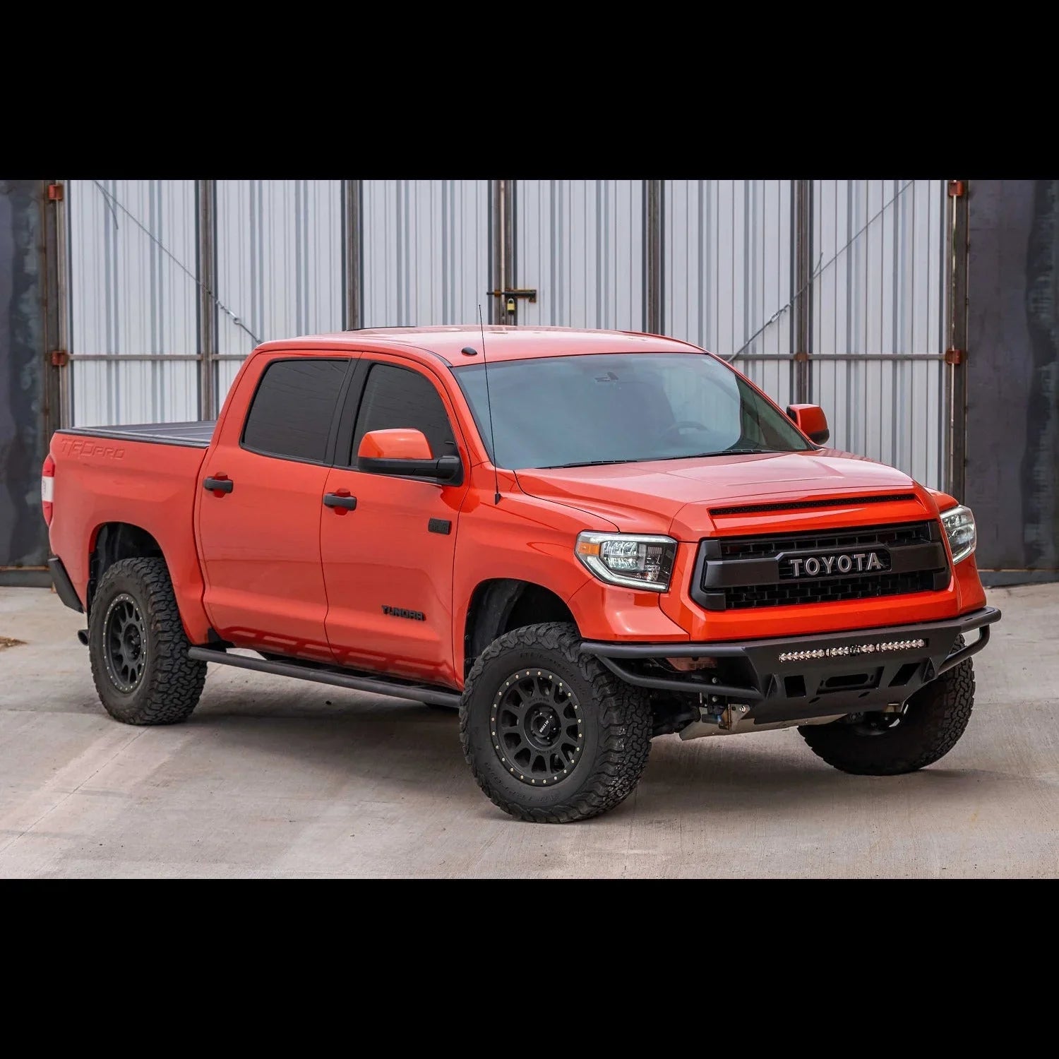 Lifted orange Toyota Tundra off-road truck with custom wheels and front bumper, parked outdoors