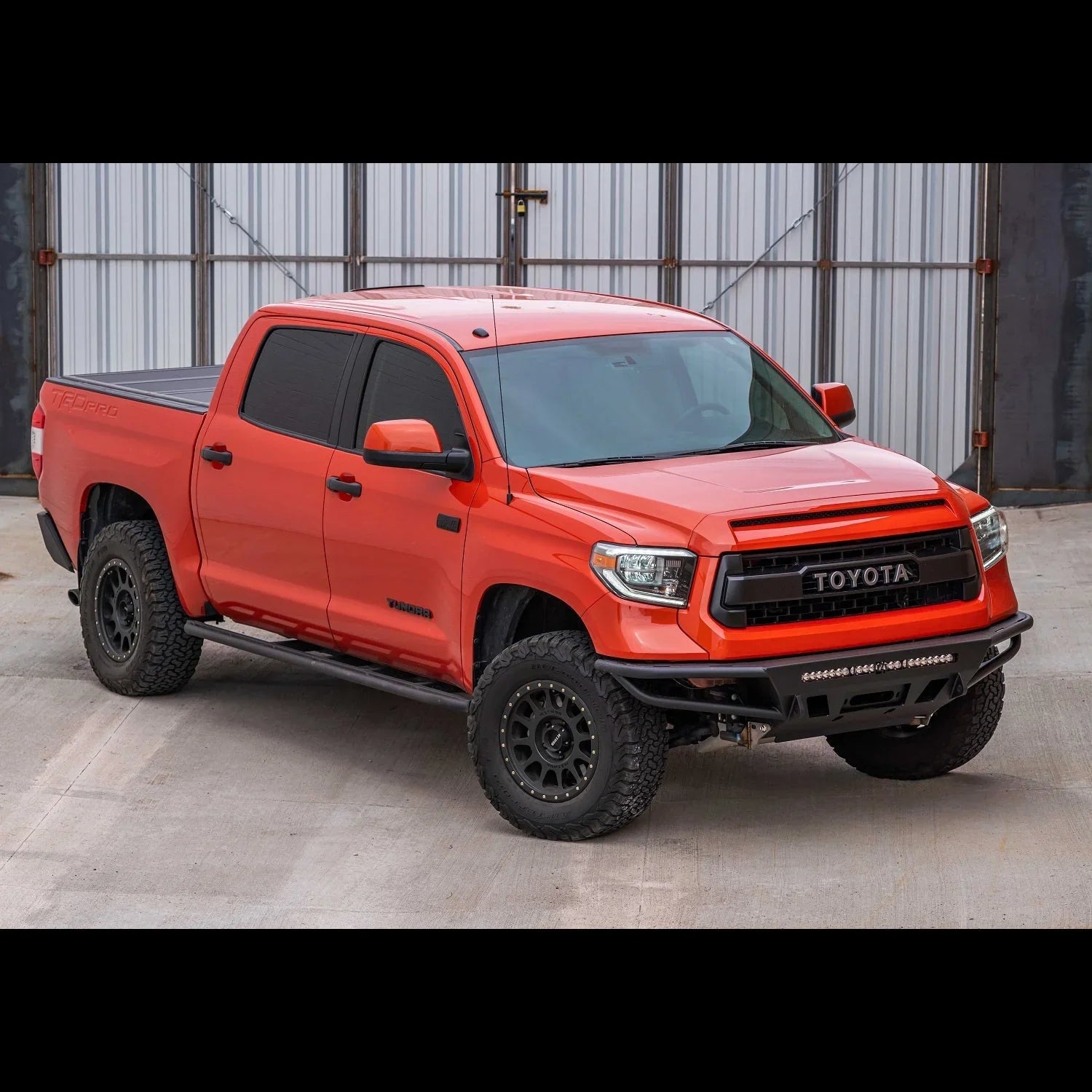 Toyota Tundra TRD Pro in orange with off-road tires, aftermarket bumper, and rock sliders