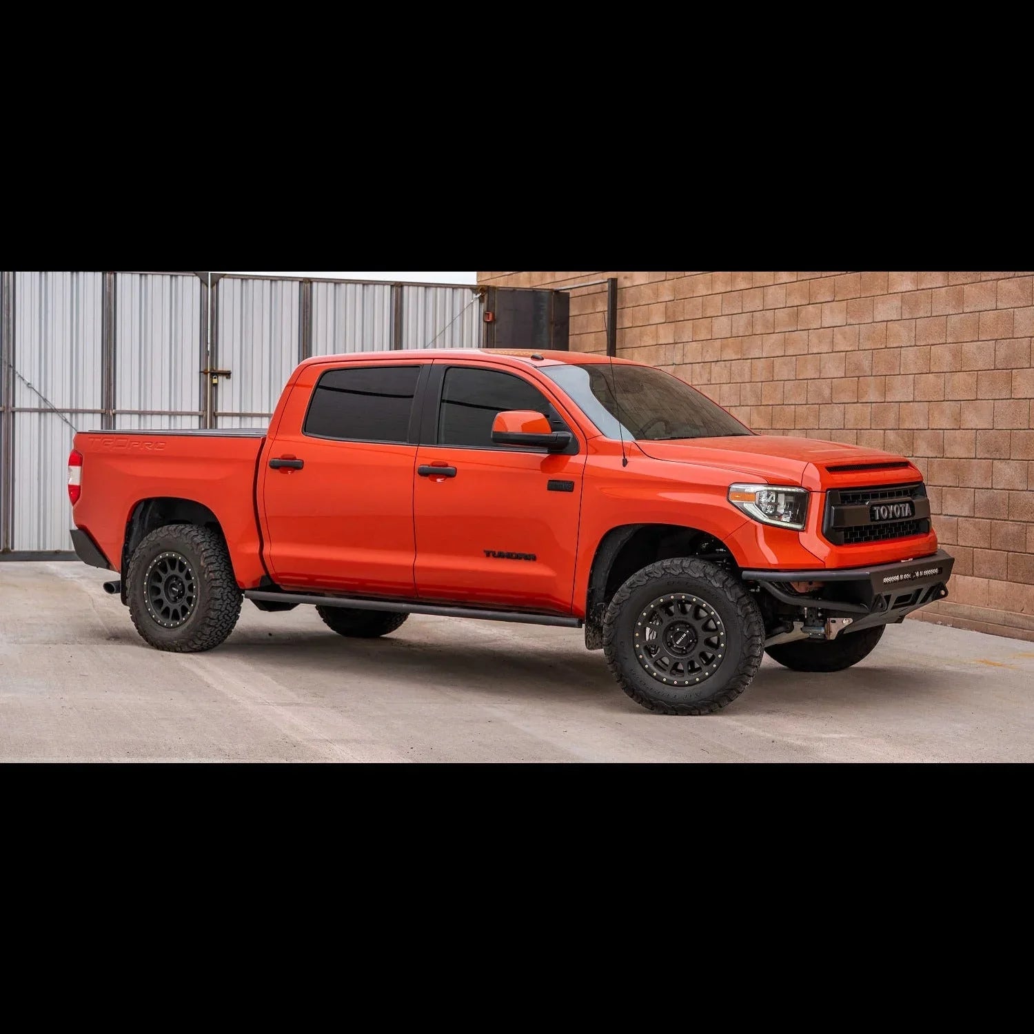 Lifted orange Toyota Tundra pickup truck with off-road tires parked by a brick wall