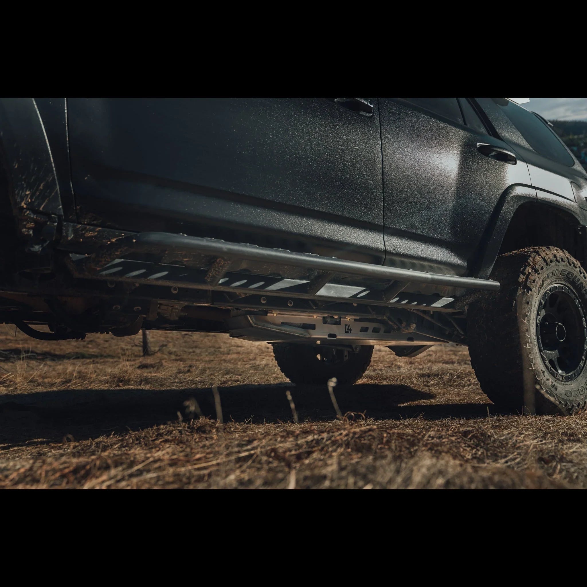 Off-road truck with metal rock sliders and skid plate, parked on rugged outdoor terrain