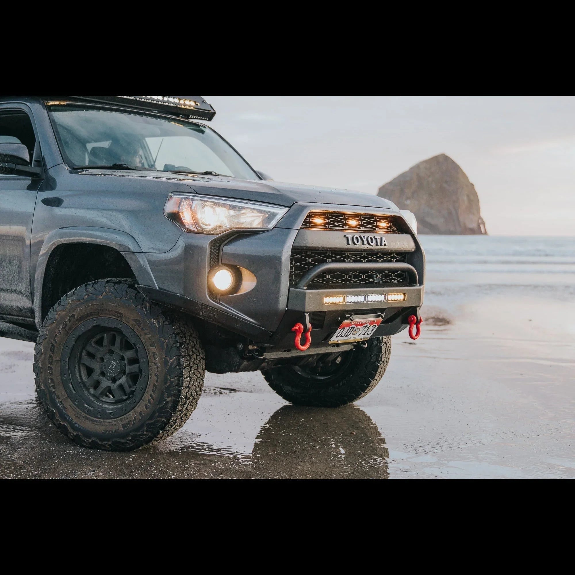 Toyota 4Runner with off-road bumper and accessories parked on beach, sea stack in background