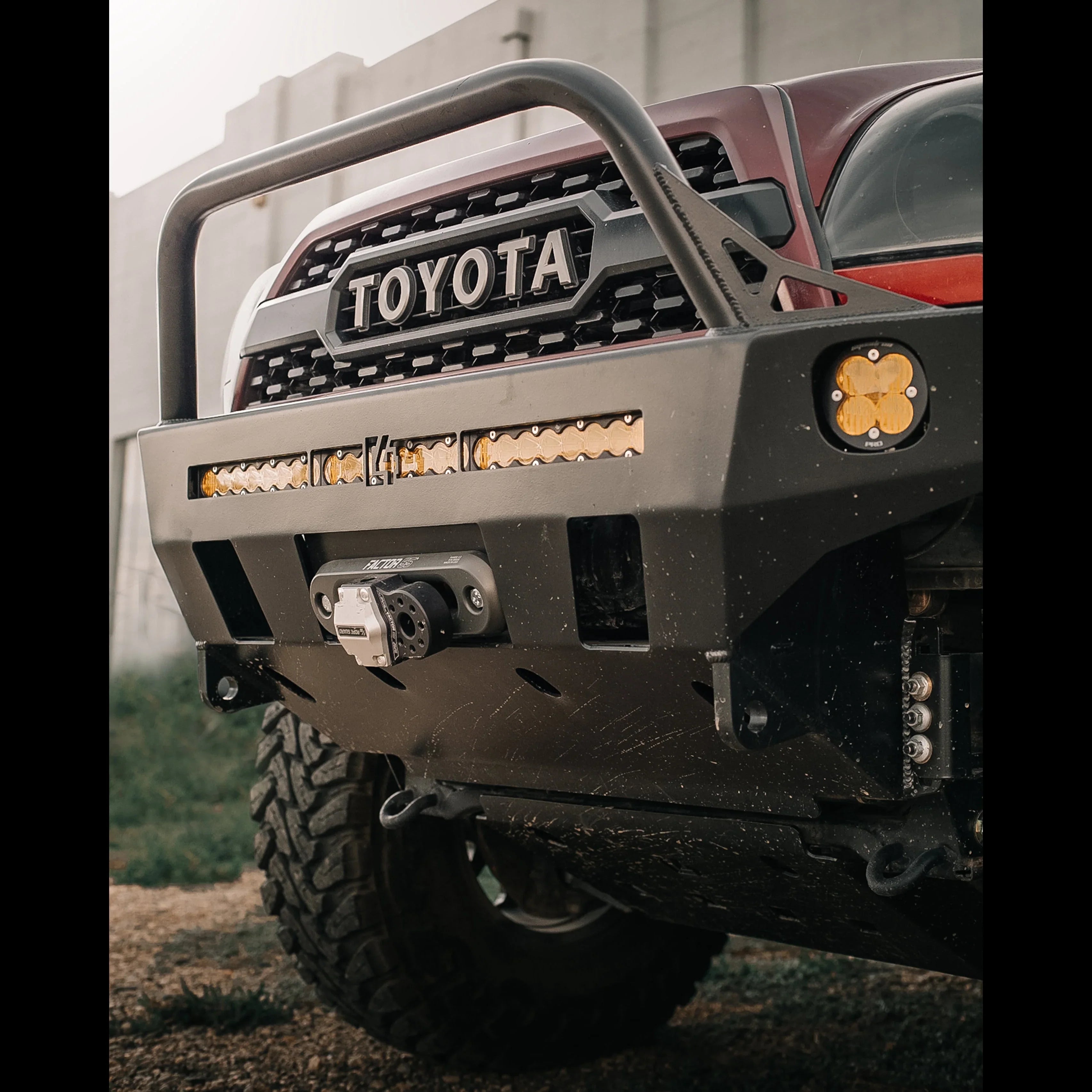 Toyota Tacoma with off-road front bumper, LED lights, and winch on rugged terrain