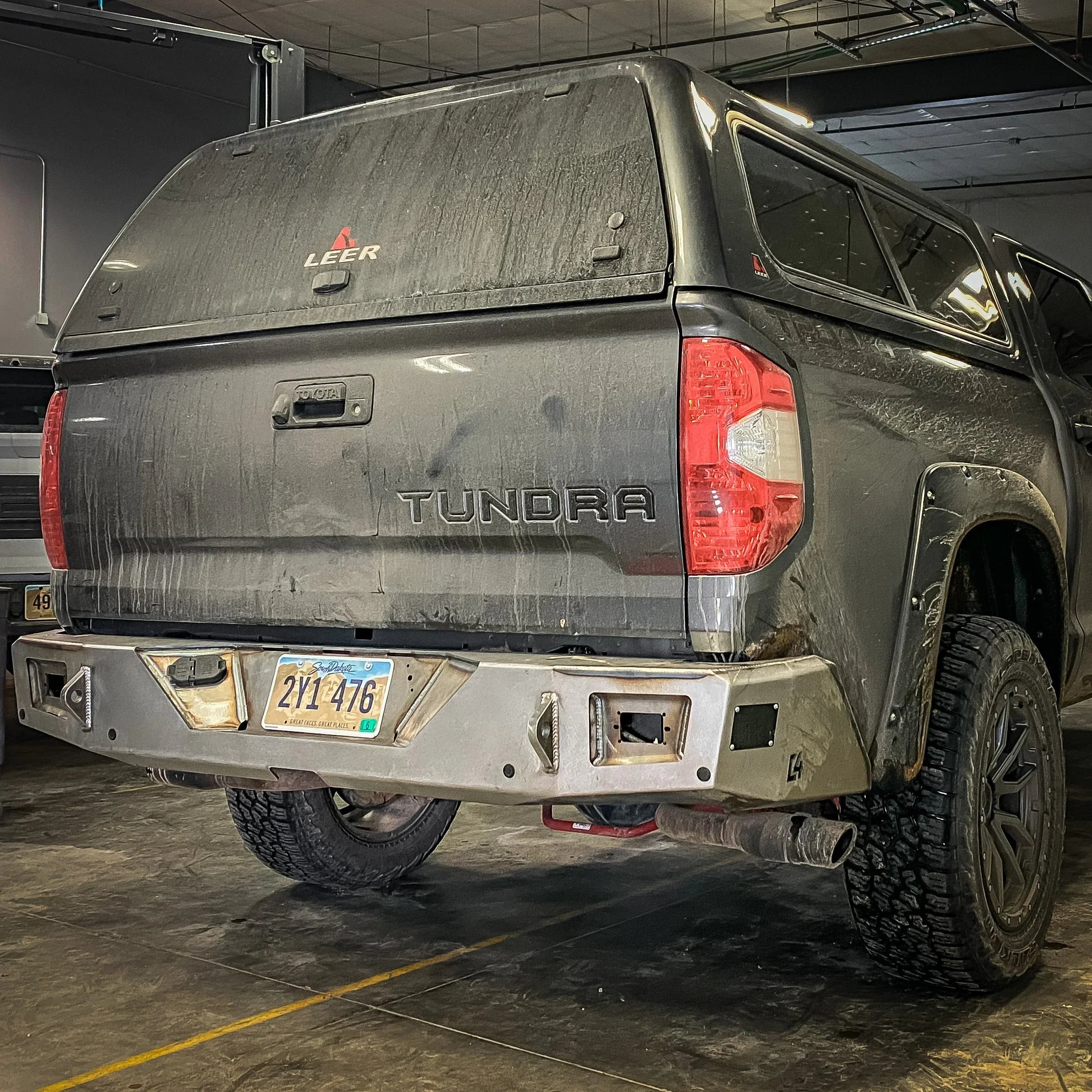 Toyota Tundra with aftermarket rear bumper, topper, and off-road tires in a garage