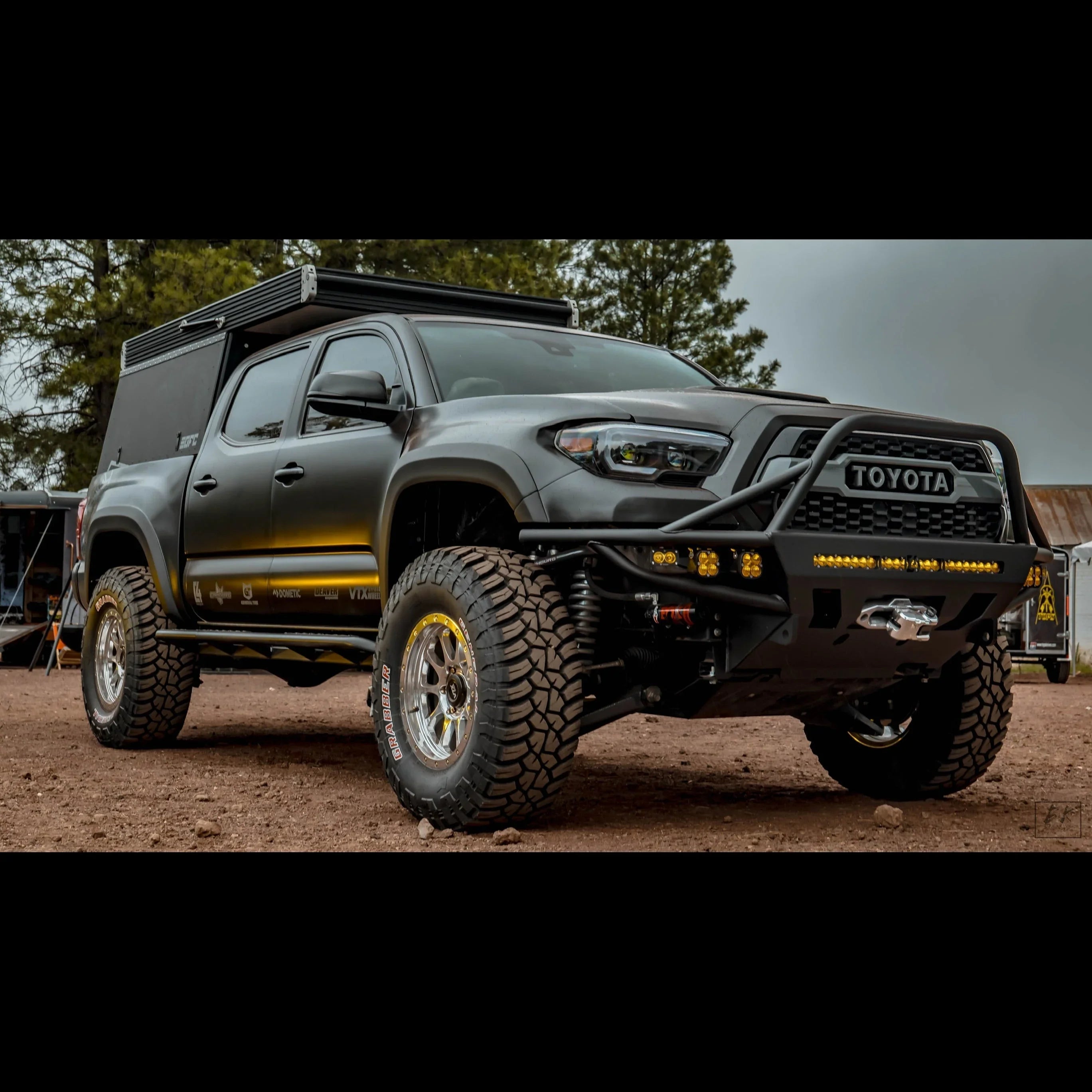 Lifted Toyota Tacoma overlanding truck with off-road tires, custom bumper, roof tent, and trail gear